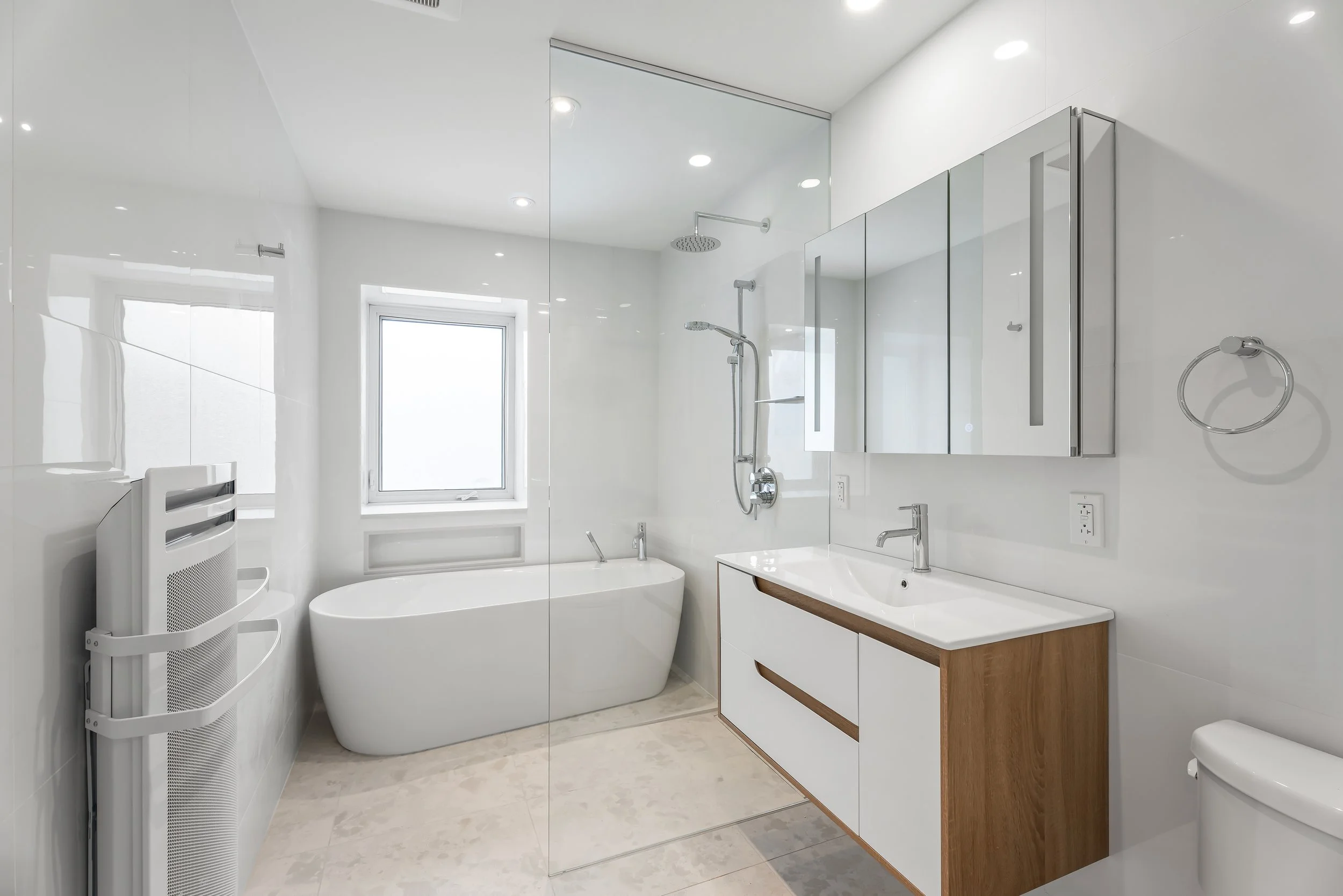 Bathroom renovation in Montreal featuring a clean, modern layout with floating vanity, medicine cabinet, and freestanding tub in wet room. 