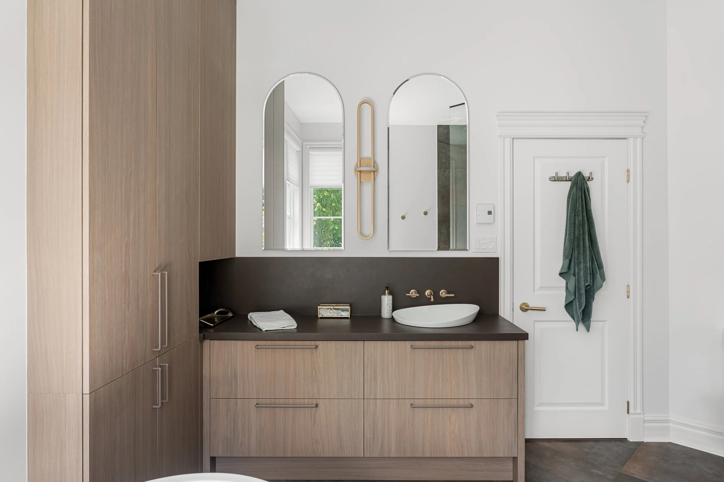 Custom bathroom vanity renovation in Montreal featuring wood cabinetry, vessel sink, and arched mirrors.