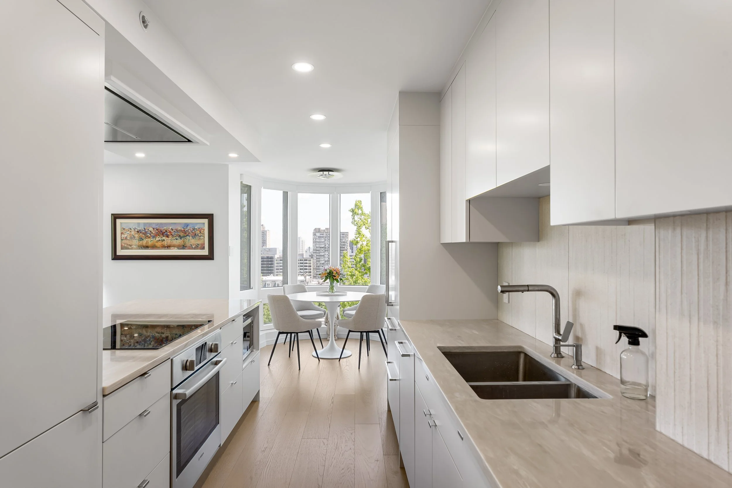 Luxury residential condo renovation in Montreal featuring a modern white galley kitchen with quartz countertops. 