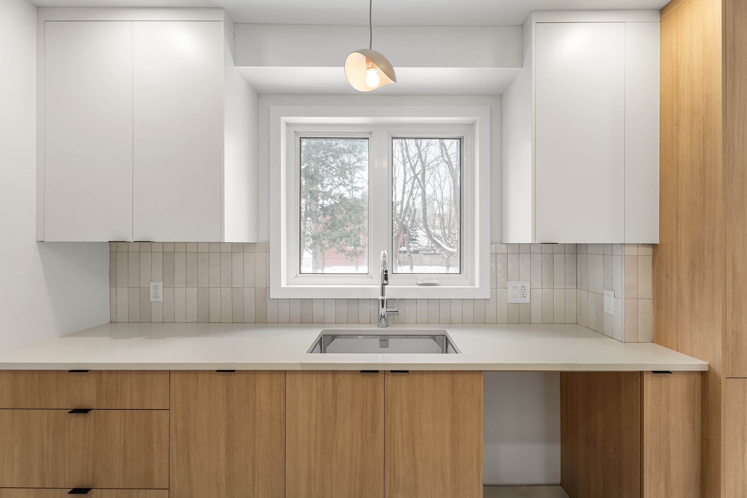 Residential renovation in Montreal featuring custom oak and cream cabinets with a pendant light fixture and undermount sink. 