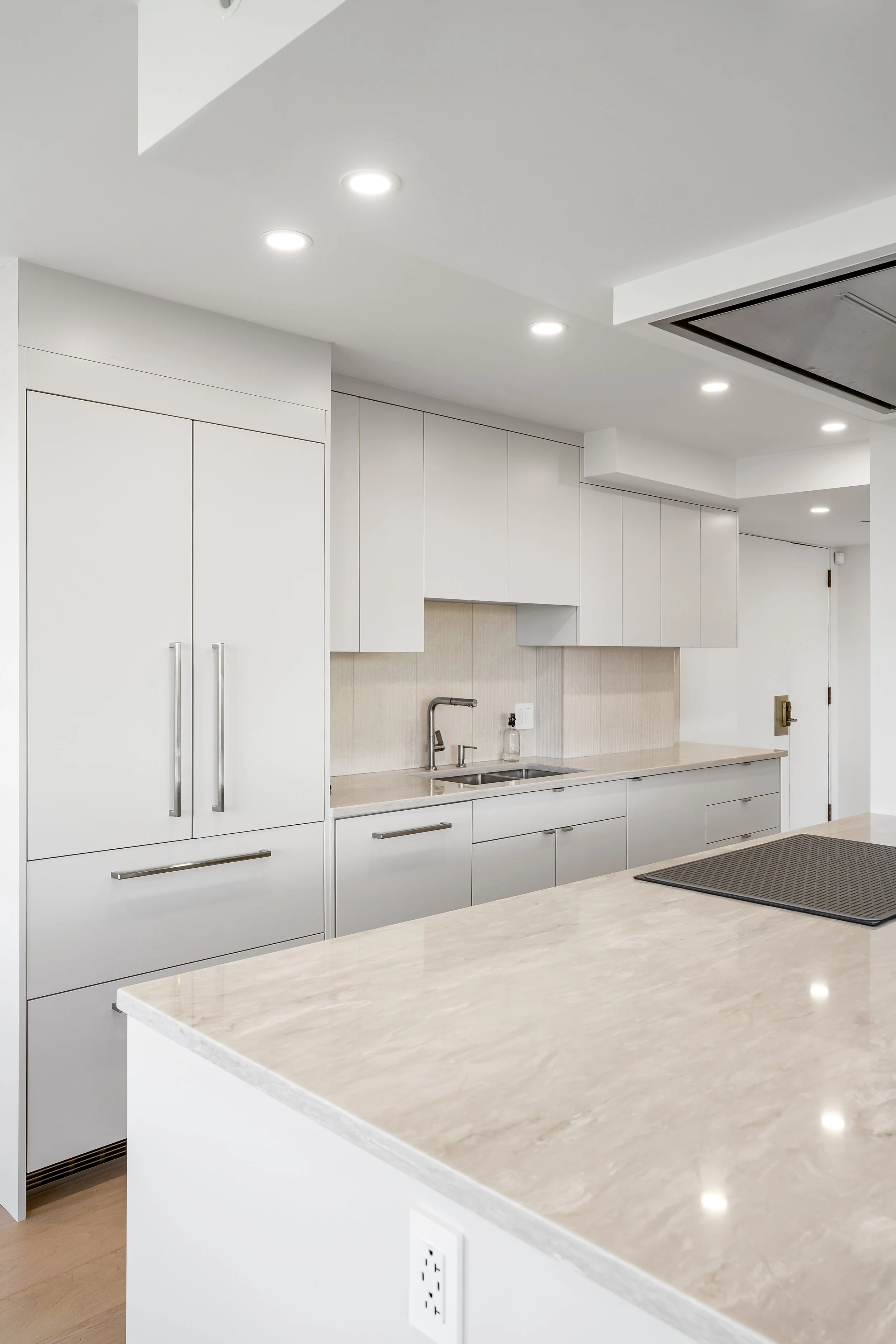 High-end condo kitchen renovation on Atwater in Montreal featuring custom lacquered off-white cabinetry, integrated lighting, and a peninsula with cooktop and recessed ceiling fan.