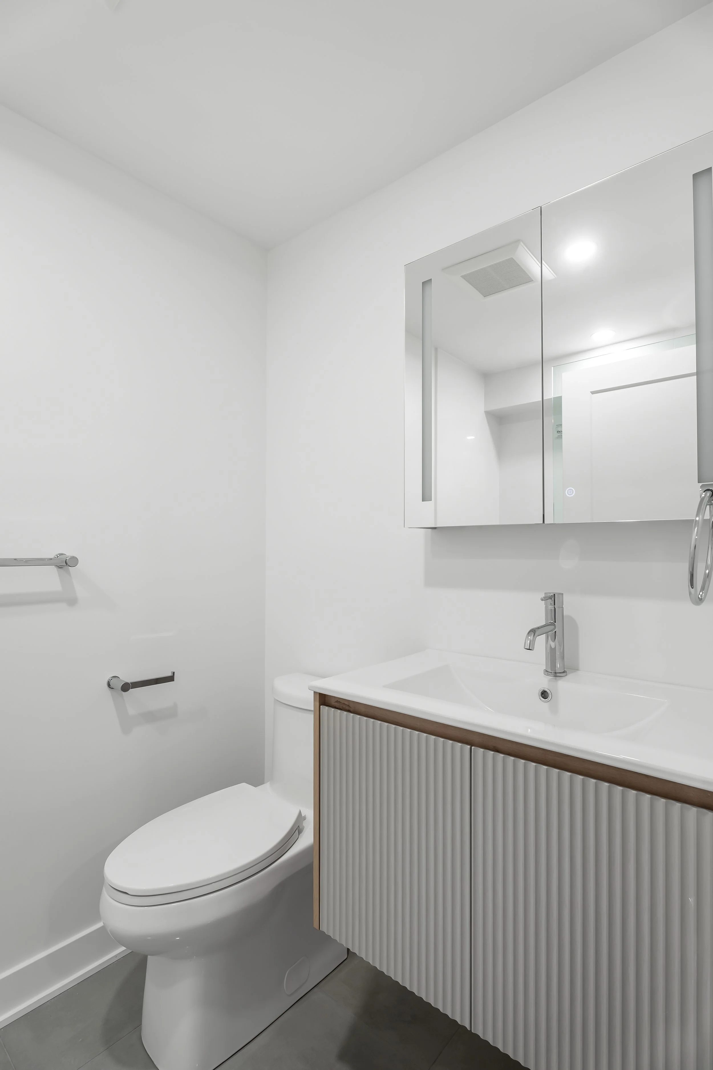 Basement bathroom renovation in Montreal featuring a floating grey vanity and medicine cabinet. 