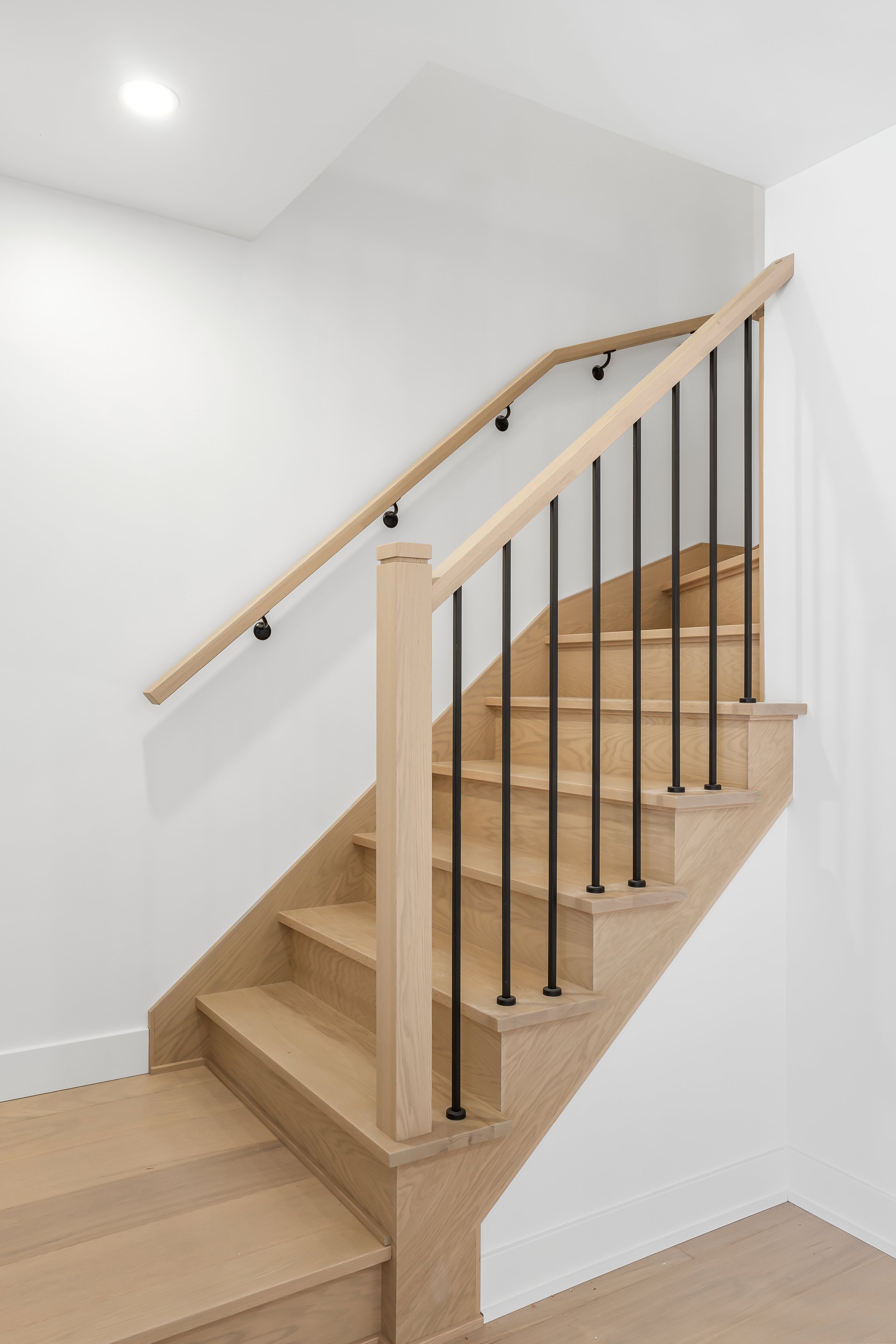 Custom staircase railing for residential renovation in Montreal with black metal balusters and oak handrail to match oak floors. 