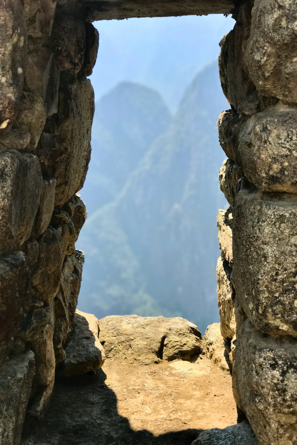 View through an opening in a stone wall showing misty mountains in the background.
