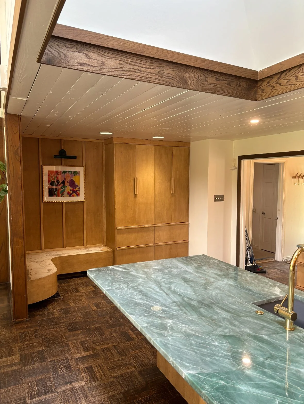 View of a kitchen with a green marble countertop, wooden cabinets, wood panel ceiling, and artwork on the wall.