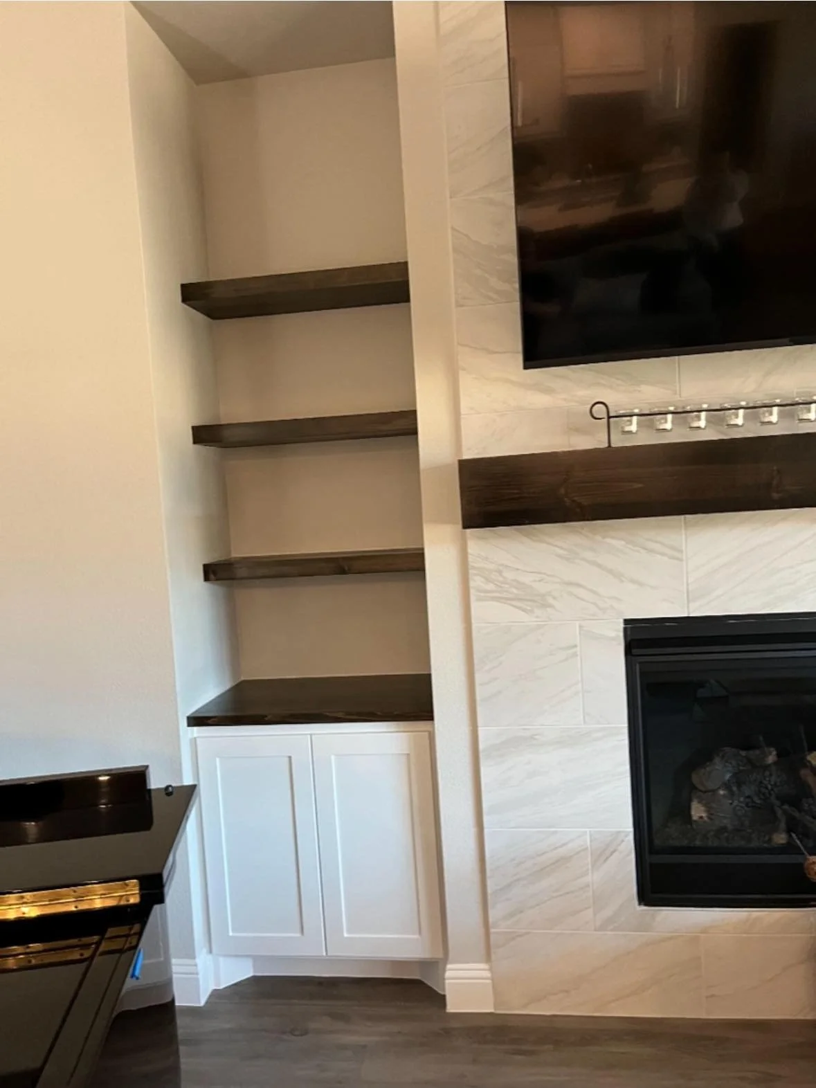 Empty built-in bookshelf with four dark wood shelves and white cabinets at the bottom, next to a fireplace and television in a living room.