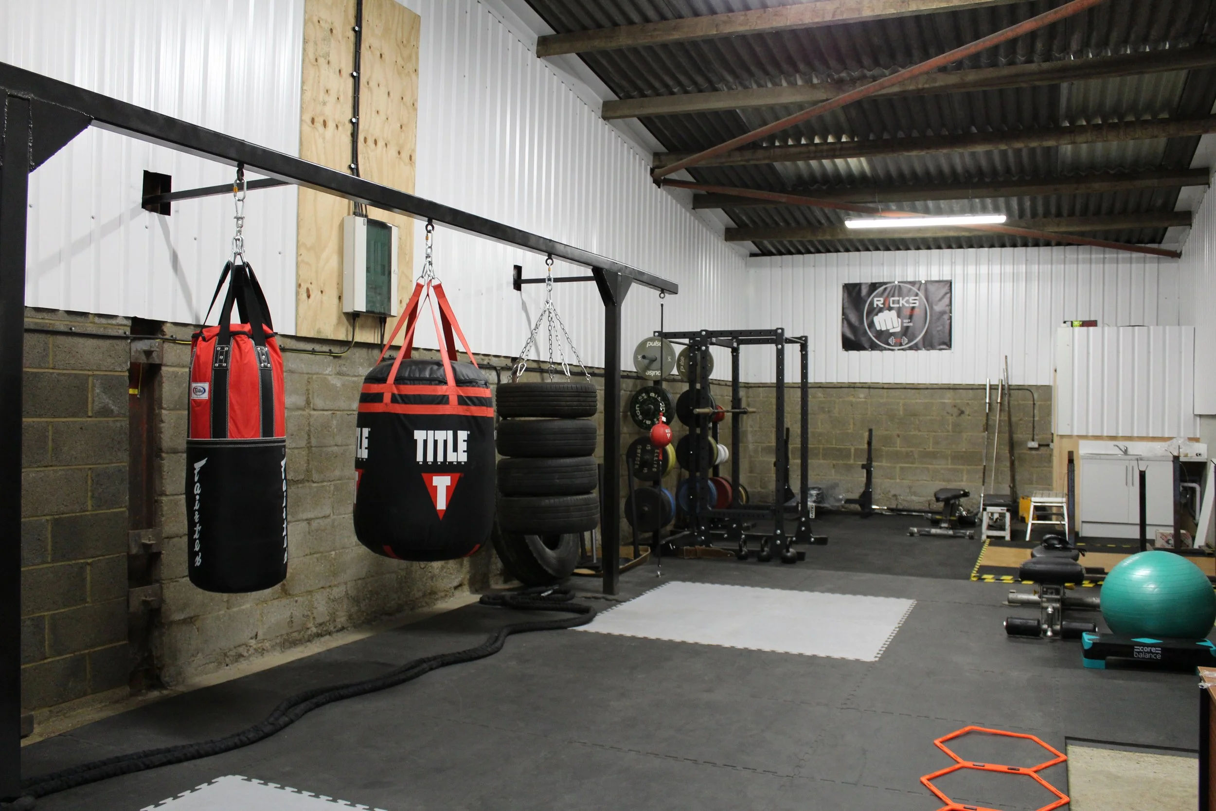 Interior of a gym with boxing bags, tires, weightlifting equipment, and exercise gear.