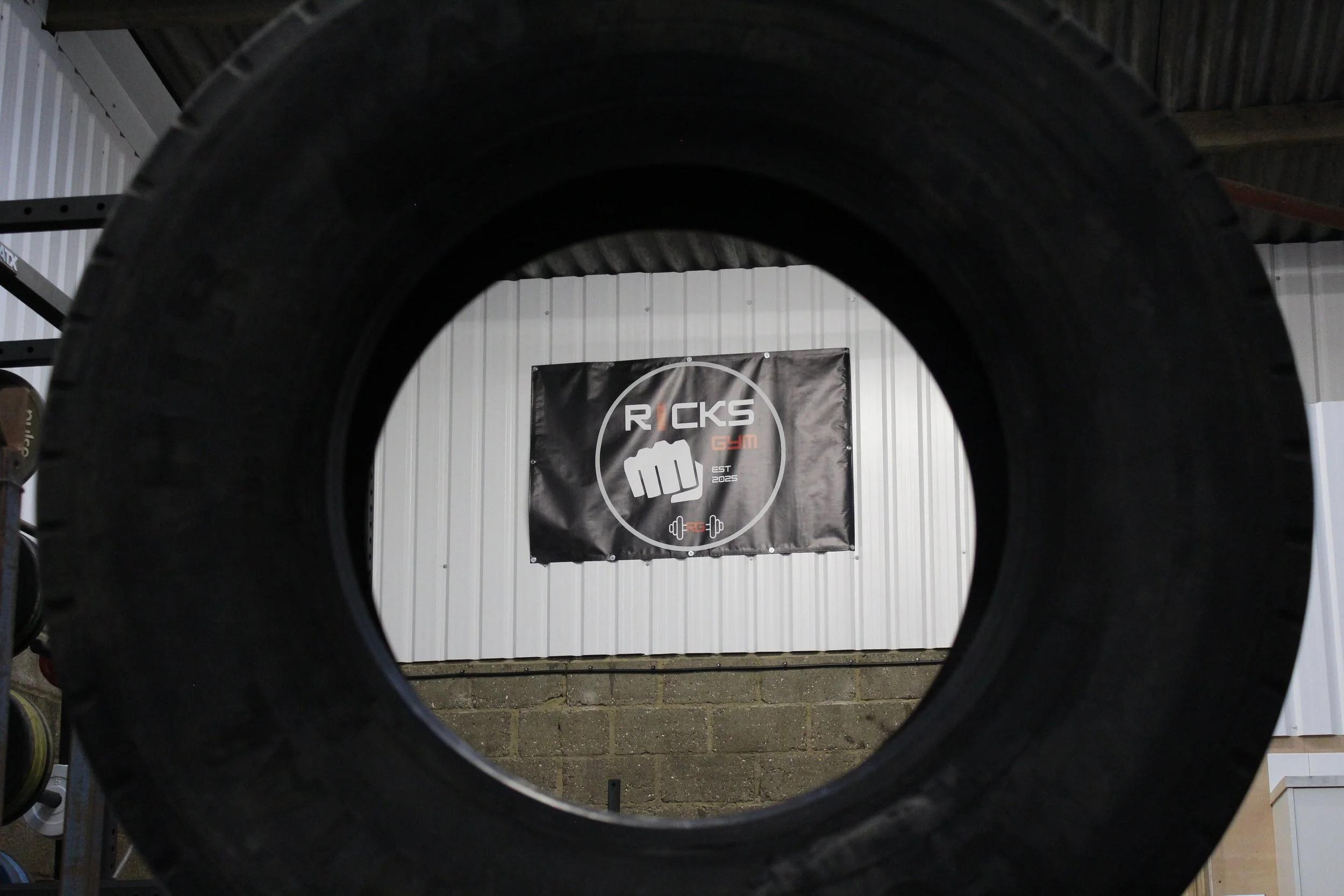 A gym with a black sign on a white wall that reads 'ROCKS GYM' with a fist icon and a barbell with weights.