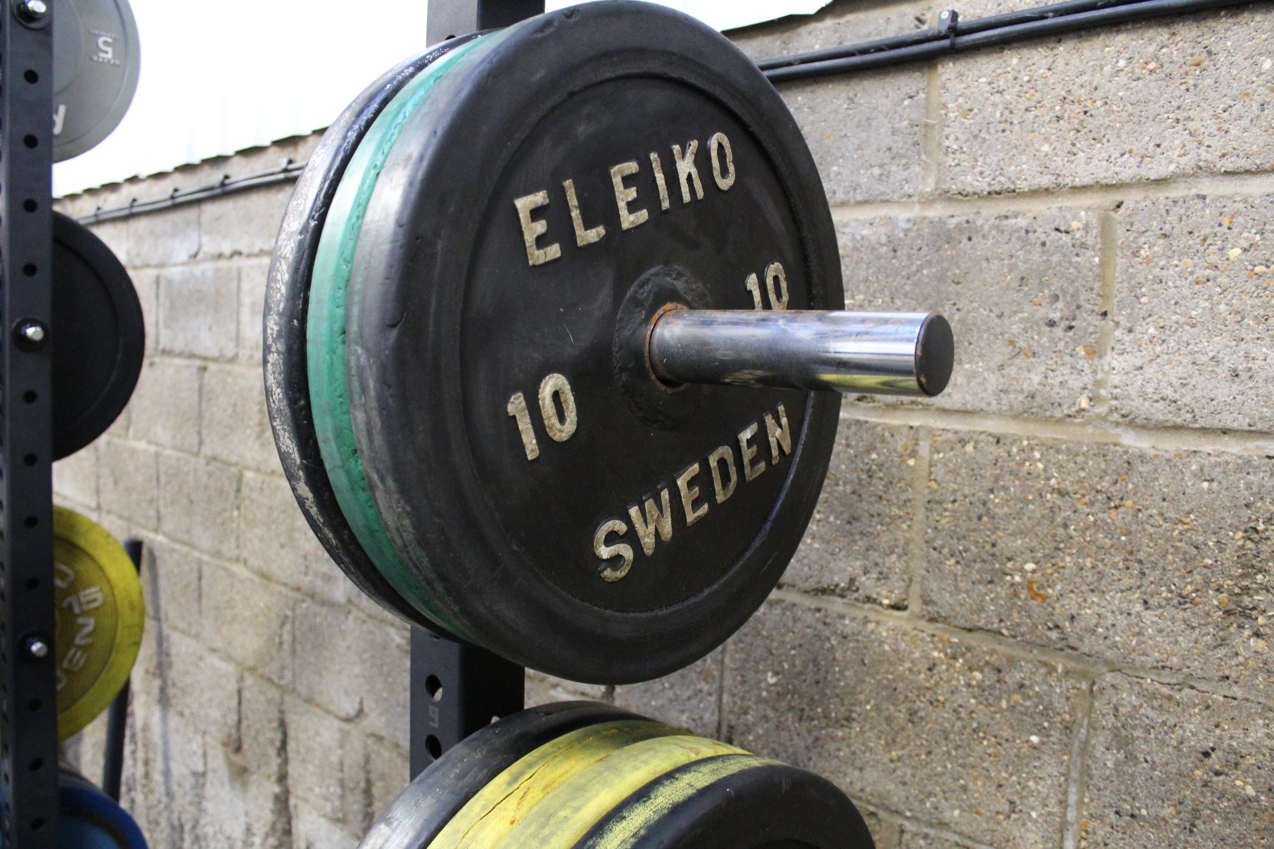 Weightlifting bumper plate on a rack with the brand name 'ELEIKO' and 'SWEDEN' printed on it.