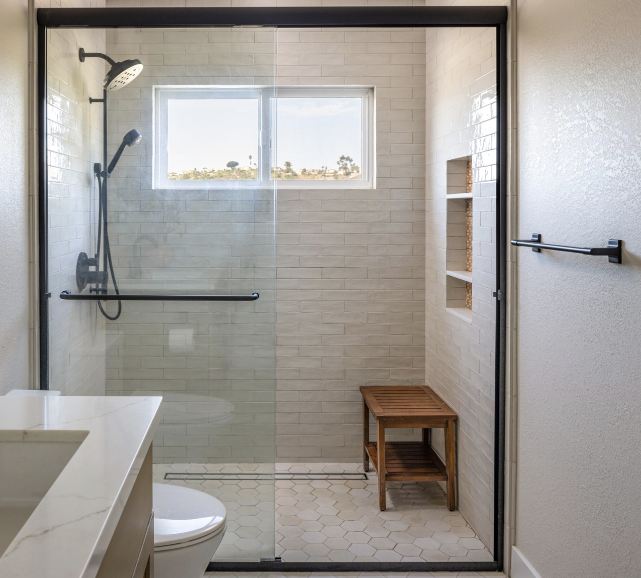 San Diego, CA bathroom design featuring a walk-in glass shower with white subway tile, hex tile flooring, and clean modern fixtures for a bright, timeless space by Anne Flynn Designs.