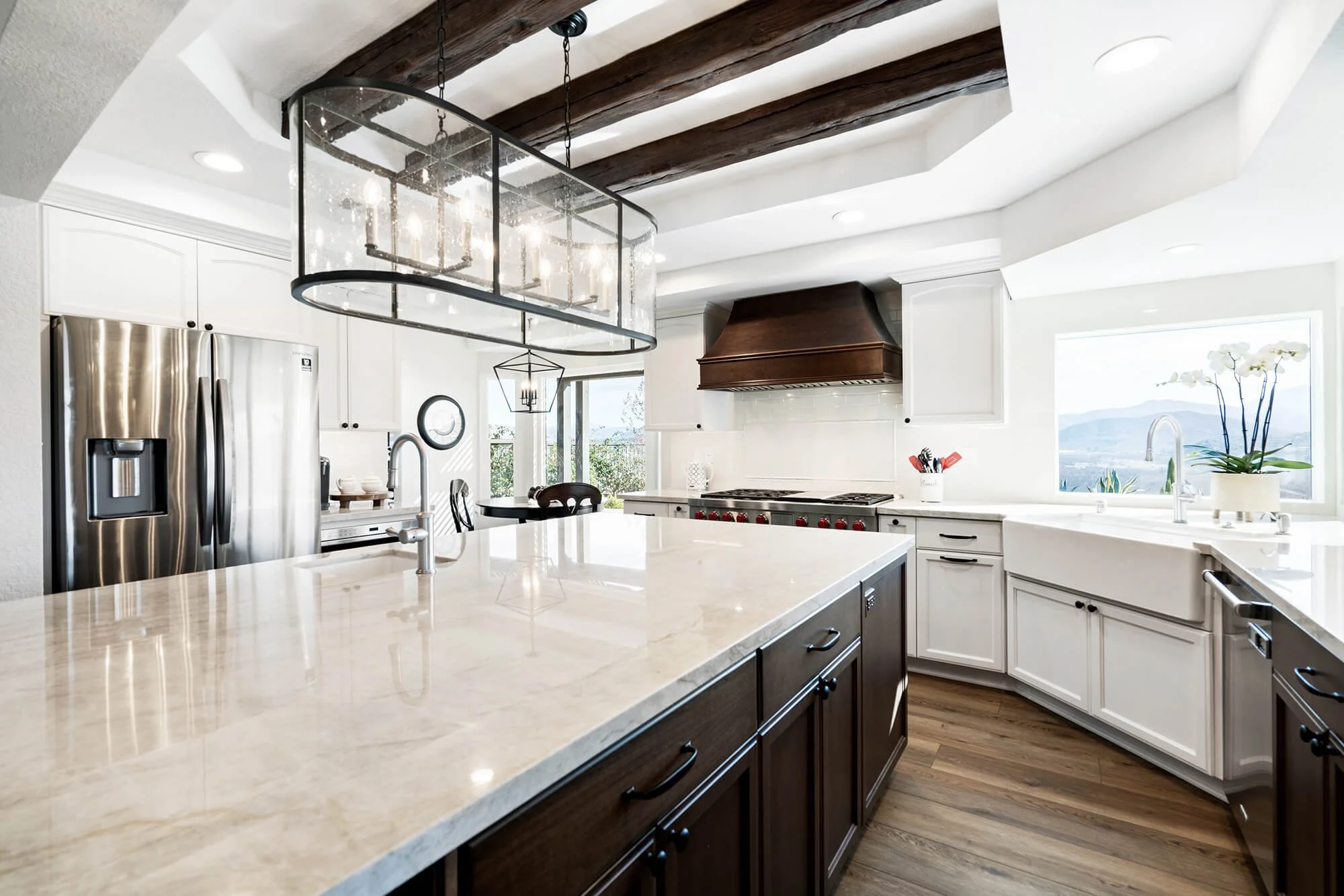 Rancho Peñasquitos, CA kitchen remodel featuring a generous stone island, custom wood range hood, exposed ceiling beams, and classic cabinetry for an elevated traditional aesthetic by Anne Flynn Designs.