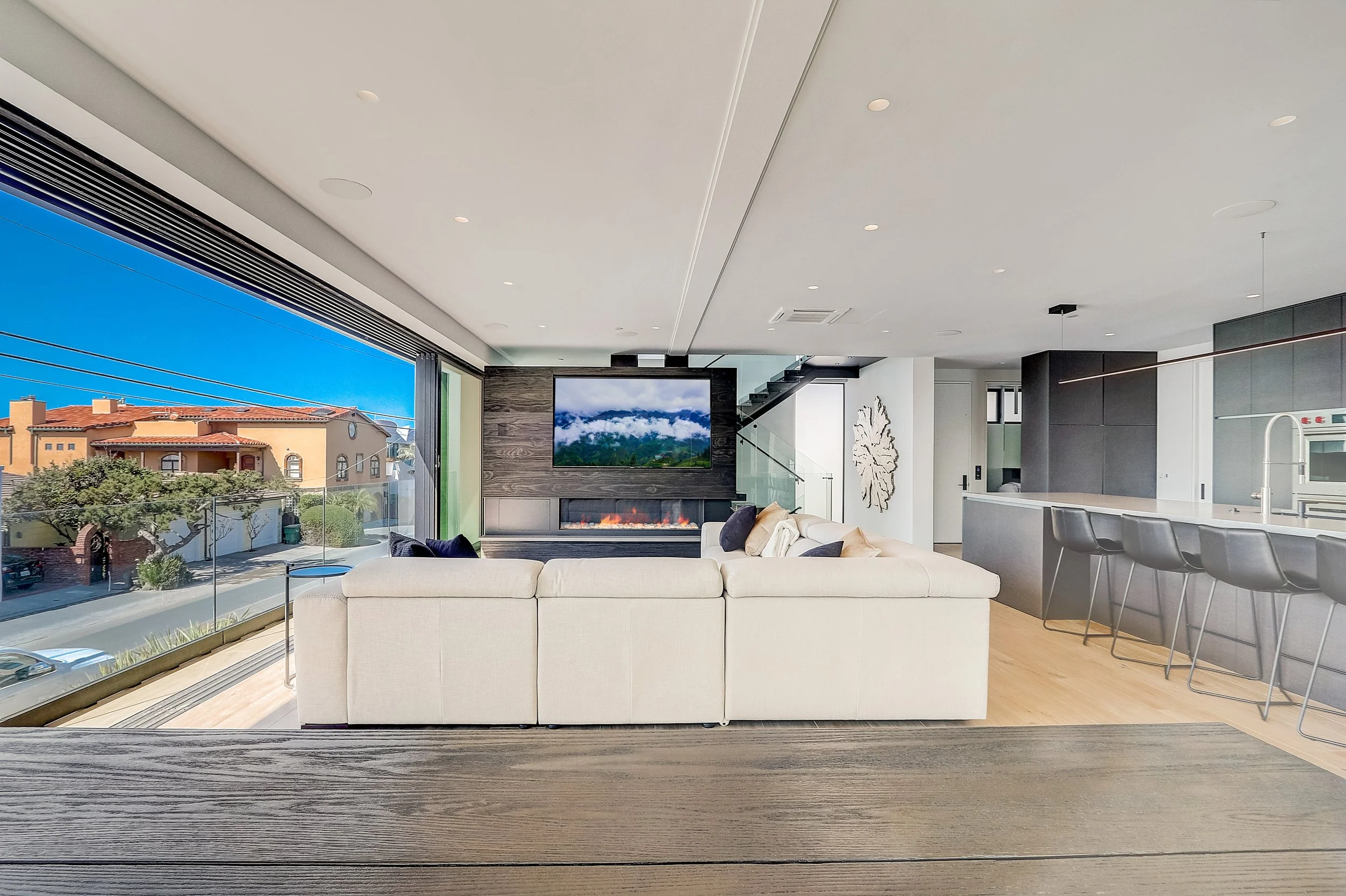 Carlsbad, CA open-concept living and kitchen design featuring expansive ocean views, a modern fireplace, and seamless indoor-outdoor living within a contemporary beach retreat by Anne Flynn Designs.