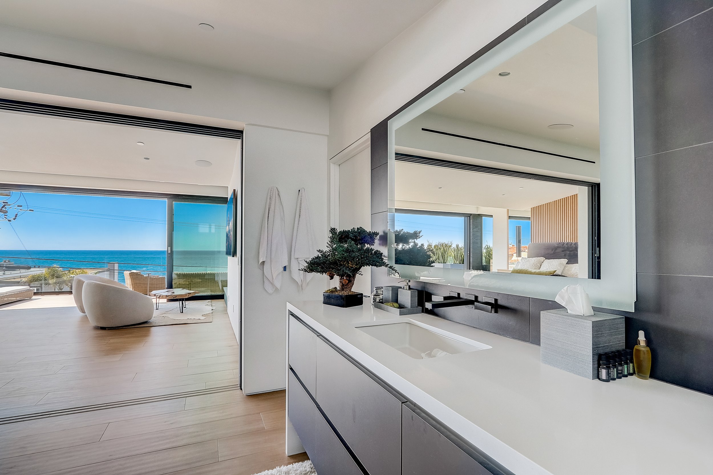 Carlsbad, CA bathroom design featuring a sleek floating vanity, integrated mirror lighting, and seamless indoor-outdoor connection with ocean views by Anne Flynn Designs.