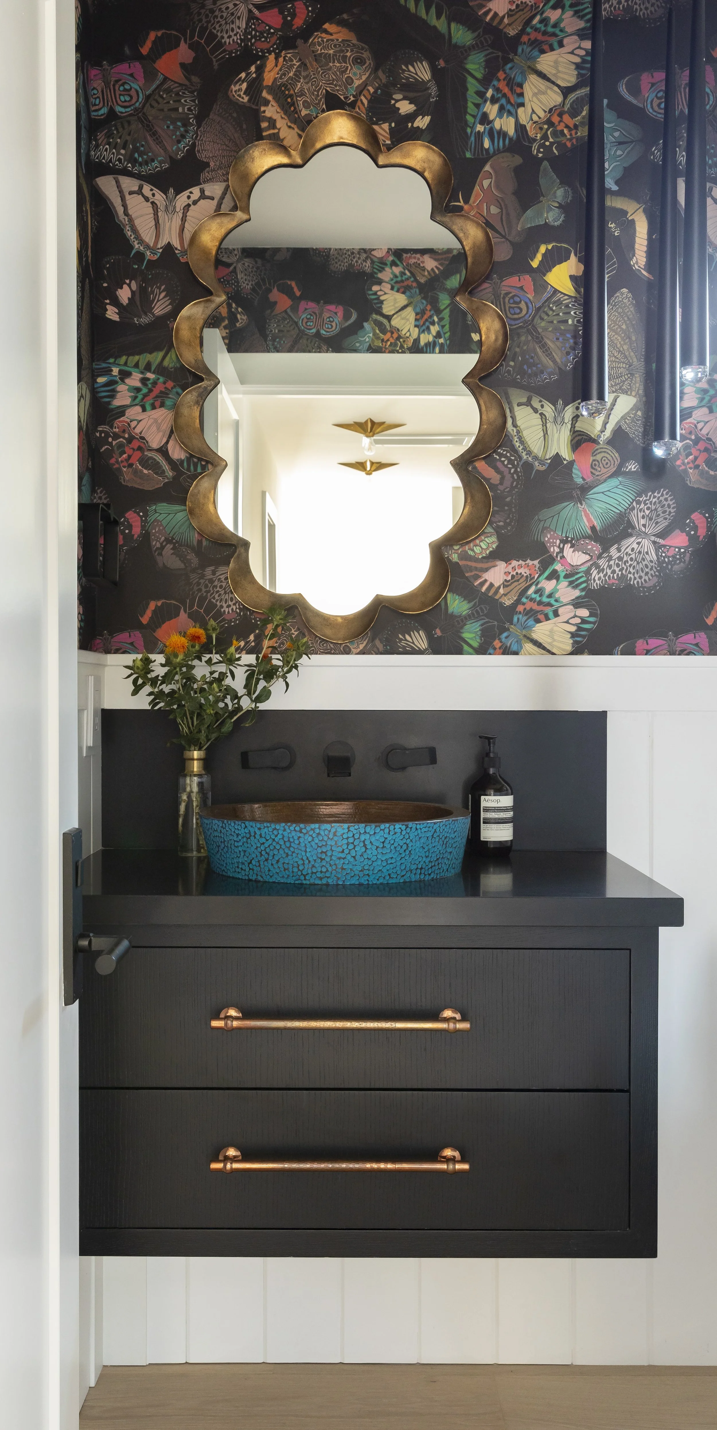 Solana Beach, CA powder room design featuring bold butterfly wallpaper, a custom vanity, sculptural mirror, and rich modern detailing by Anne Flynn Designs.