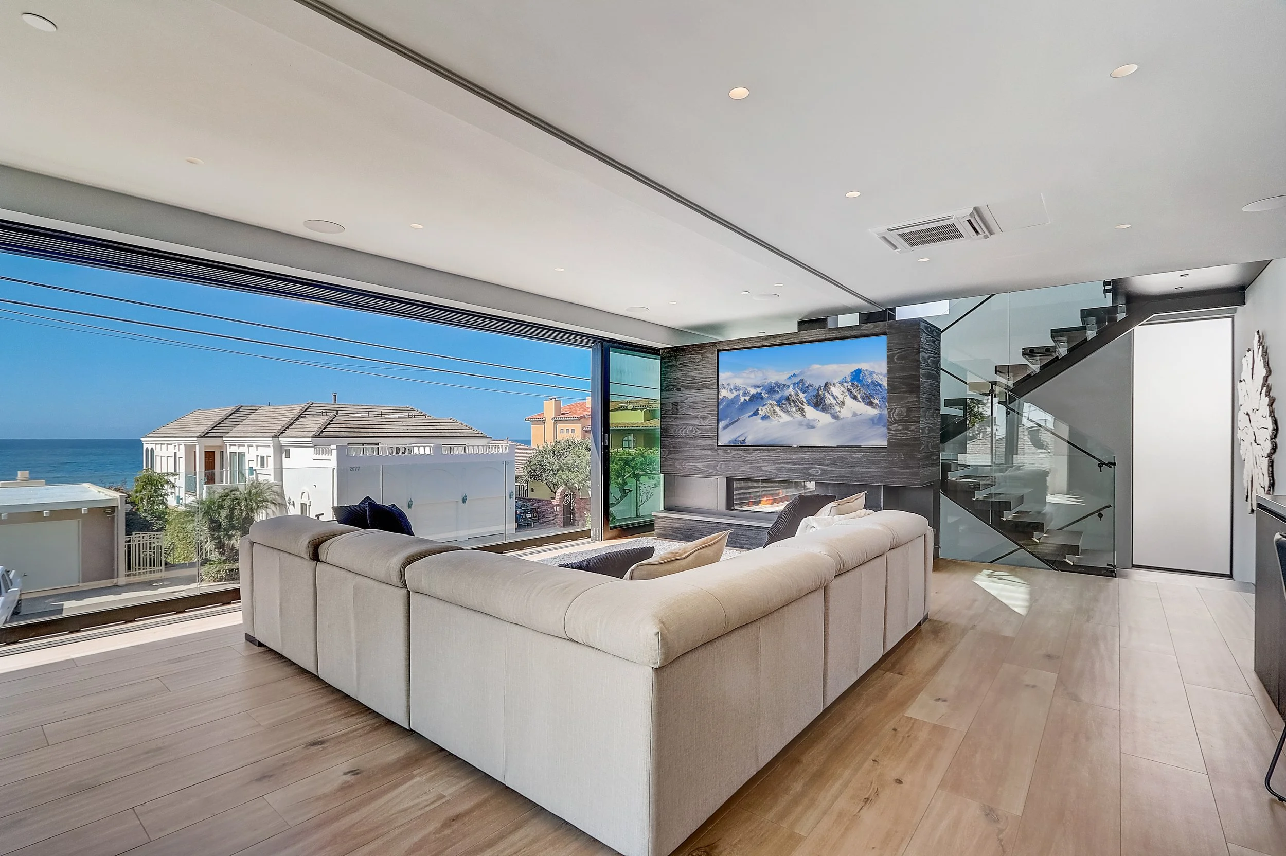 Carlsbad, CA living room design featuring expansive ocean views, a modern fireplace, glass stair railing, and clean contemporary furnishings by Anne Flynn Designs.