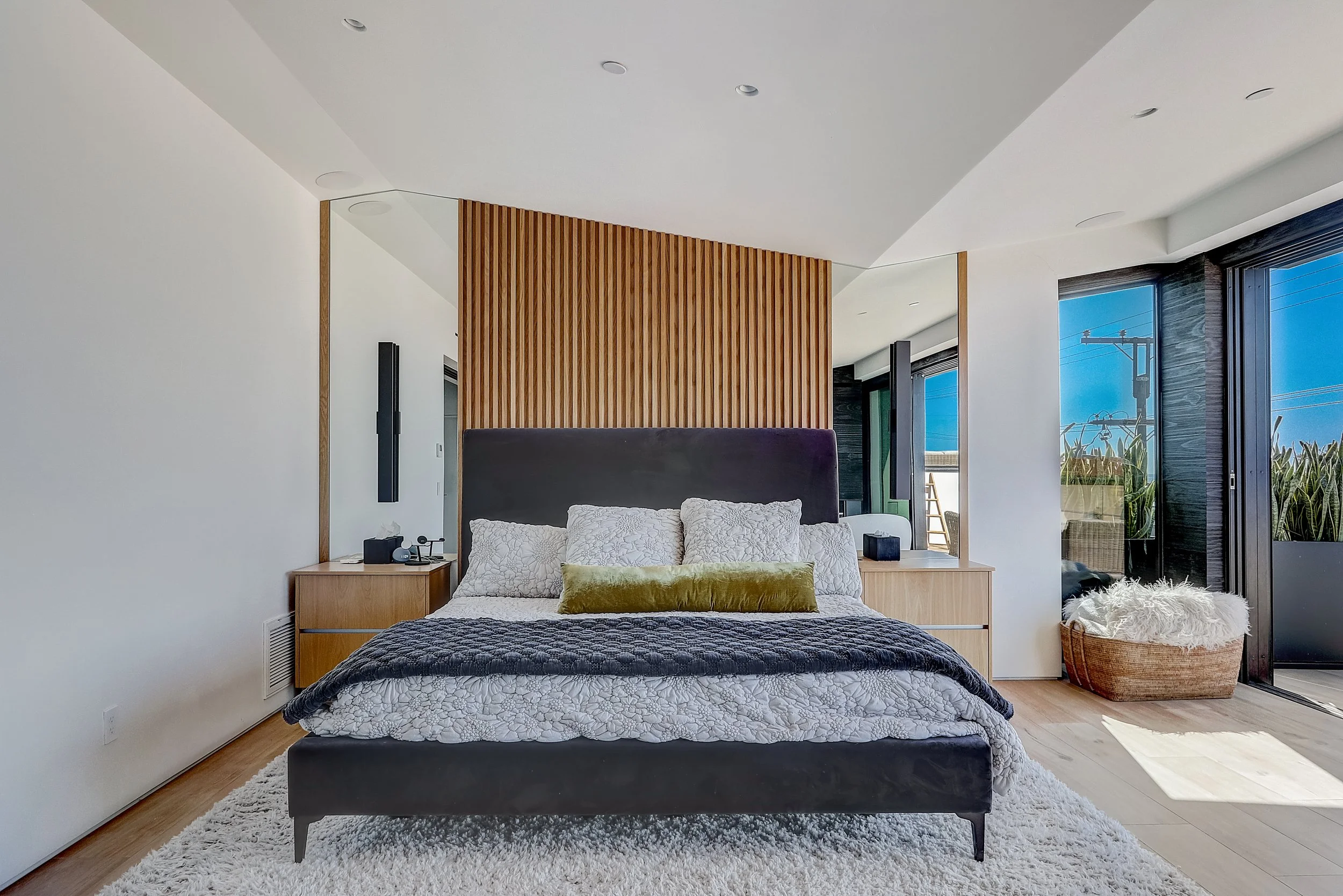 Carlsbad, CA primary bedroom design featuring a custom wood slat accent wall, tailored nightstands, and layered bedding with a clean, modern coastal aesthetic by Anne Flynn Designs.
