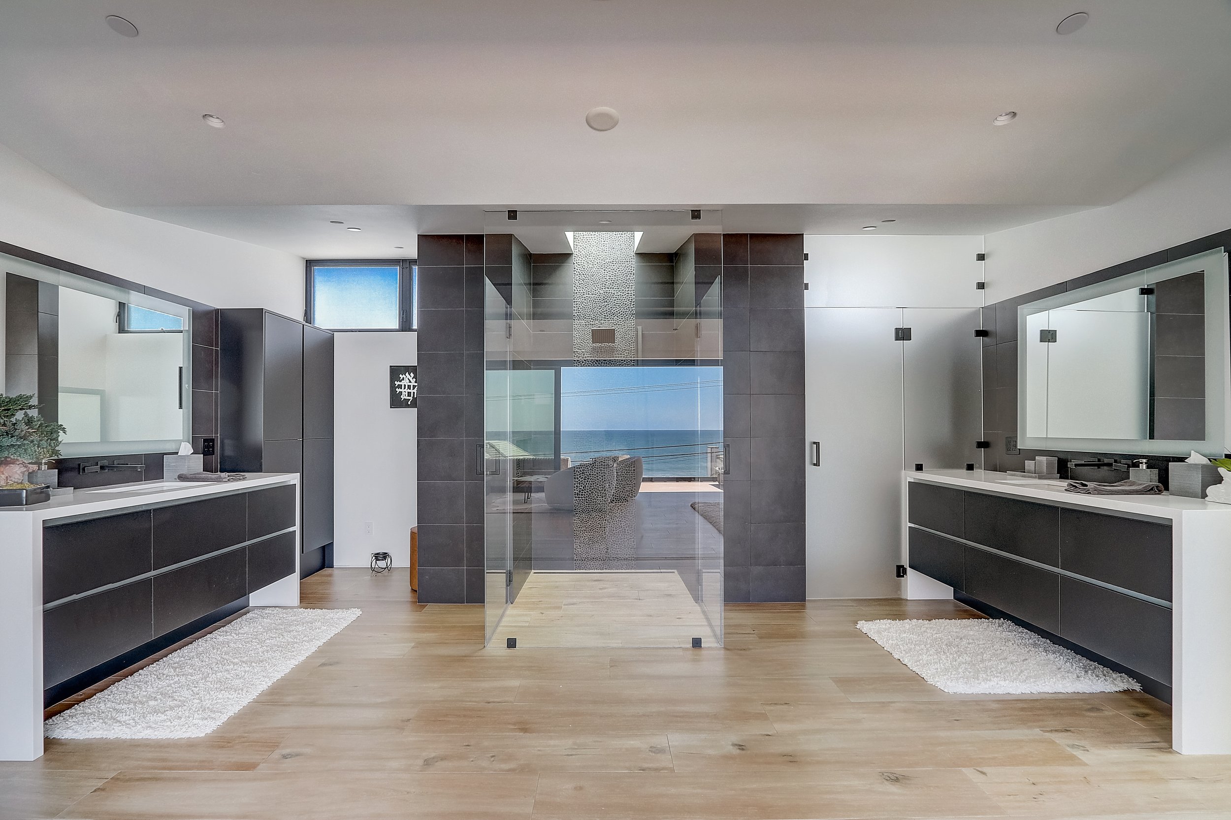 Carlsbad, CA primary bathroom design featuring dual floating vanities, a glass-enclosed walk-in shower, and clean modern finishes with ocean views by Anne Flynn Designs, architect Samuel Wright.