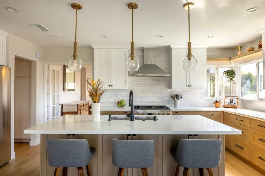 San Diego, CA kitchen design featuring a large central island, custom wood cabinetry, white quartz countertops, and warm transitional styling with modern lighting by Anne Flynn Designs.