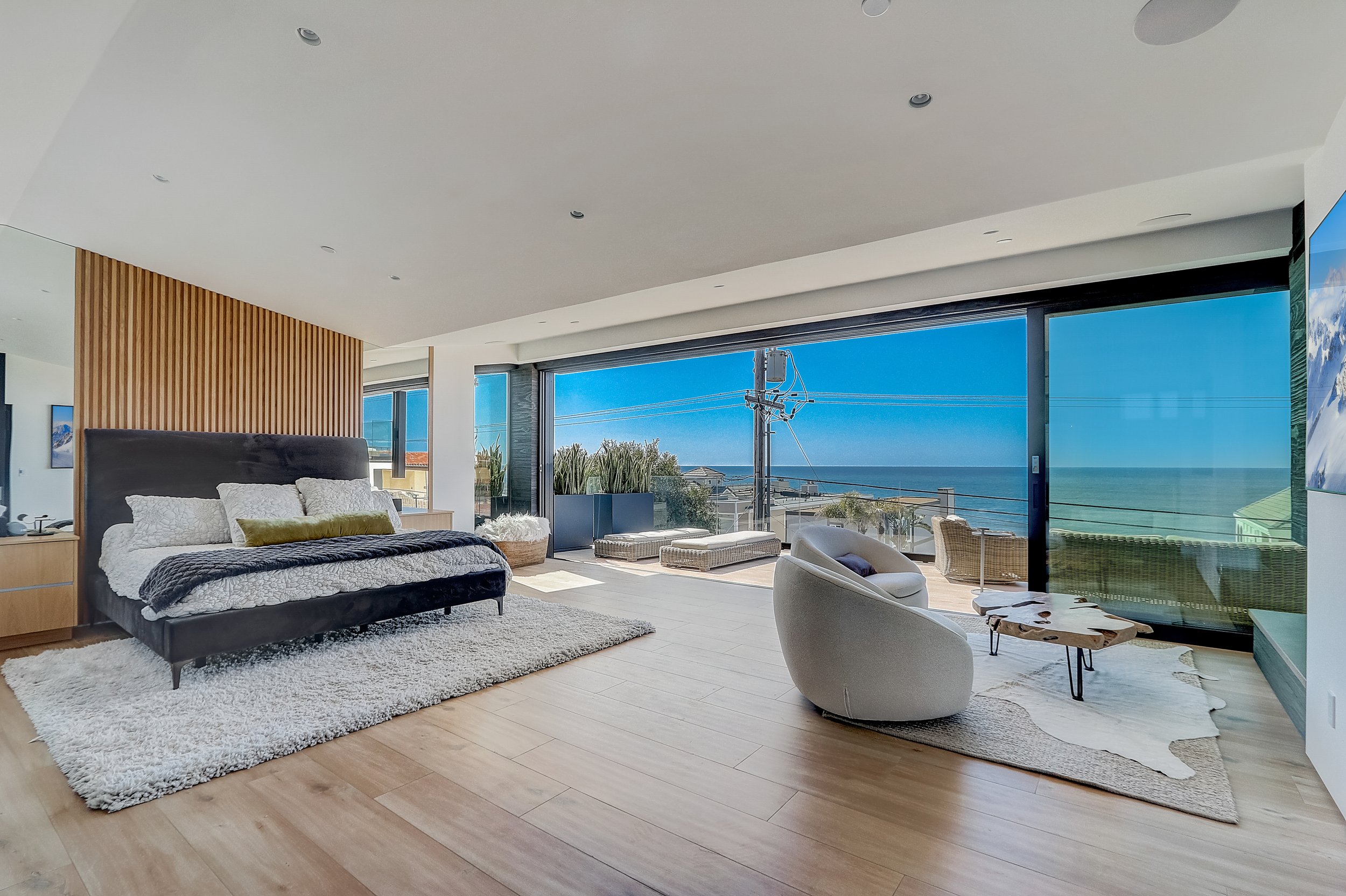 Carlsbad, CA primary bedroom design featuring expansive ocean views, floor-to-ceiling glass doors, layered textiles, and a serene modern coastal aesthetic by Anne Flynn Designs.