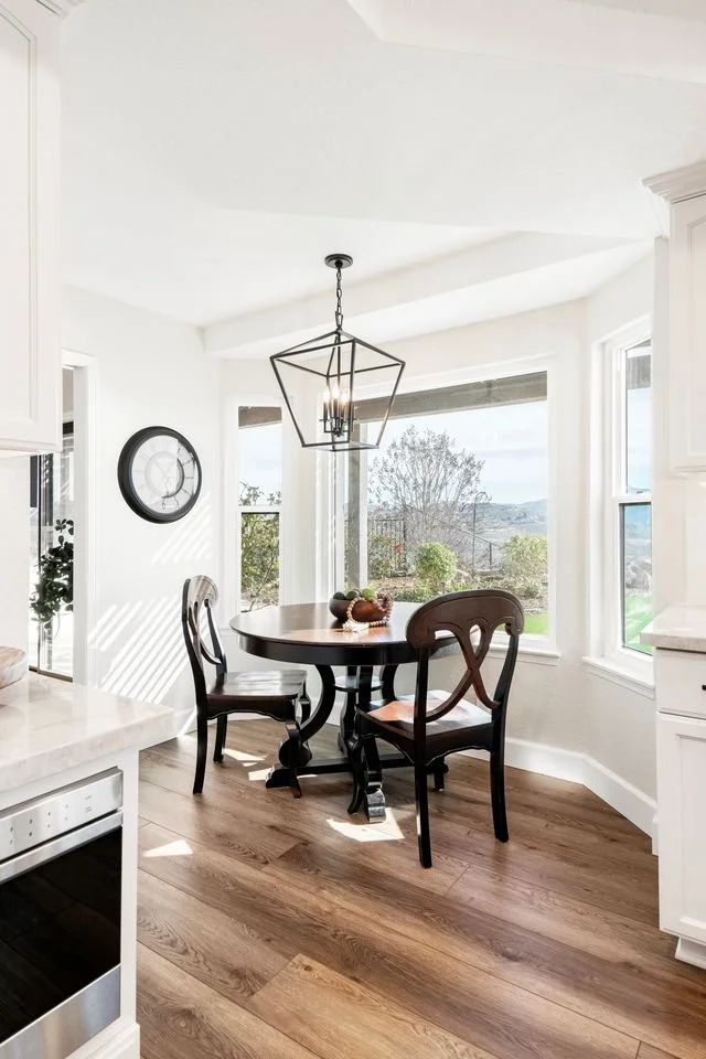 Rancho Peñasquitos, CA breakfast nook design featuring a round dining table, classic lantern-style pendant lighting, and abundant natural light with traditional detailing by Anne Flynn Designs.