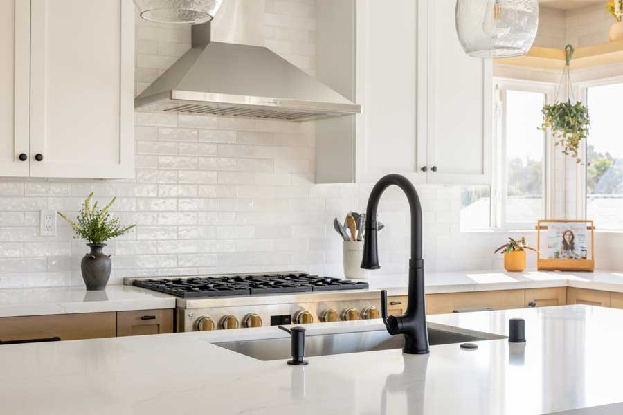 San Diego, CA kitchen design featuring a custom range with stainless steel hood, white quartz countertops, classic subway tile backsplash, and clean transitional detailing by Anne Flynn Designs.