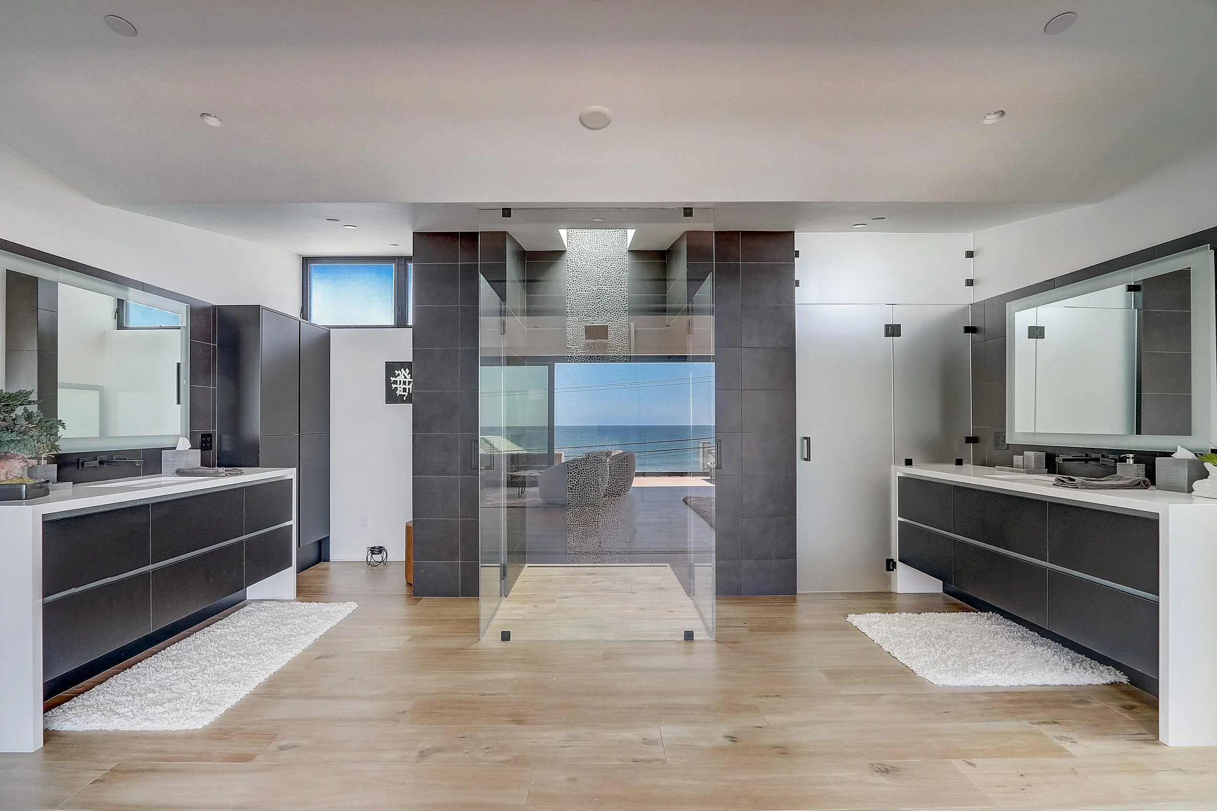 Carlsbad, CA primary bathroom design featuring dual floating vanities, a glass-enclosed walk-in shower, and clean modern finishes with ocean views by Anne Flynn Designs.