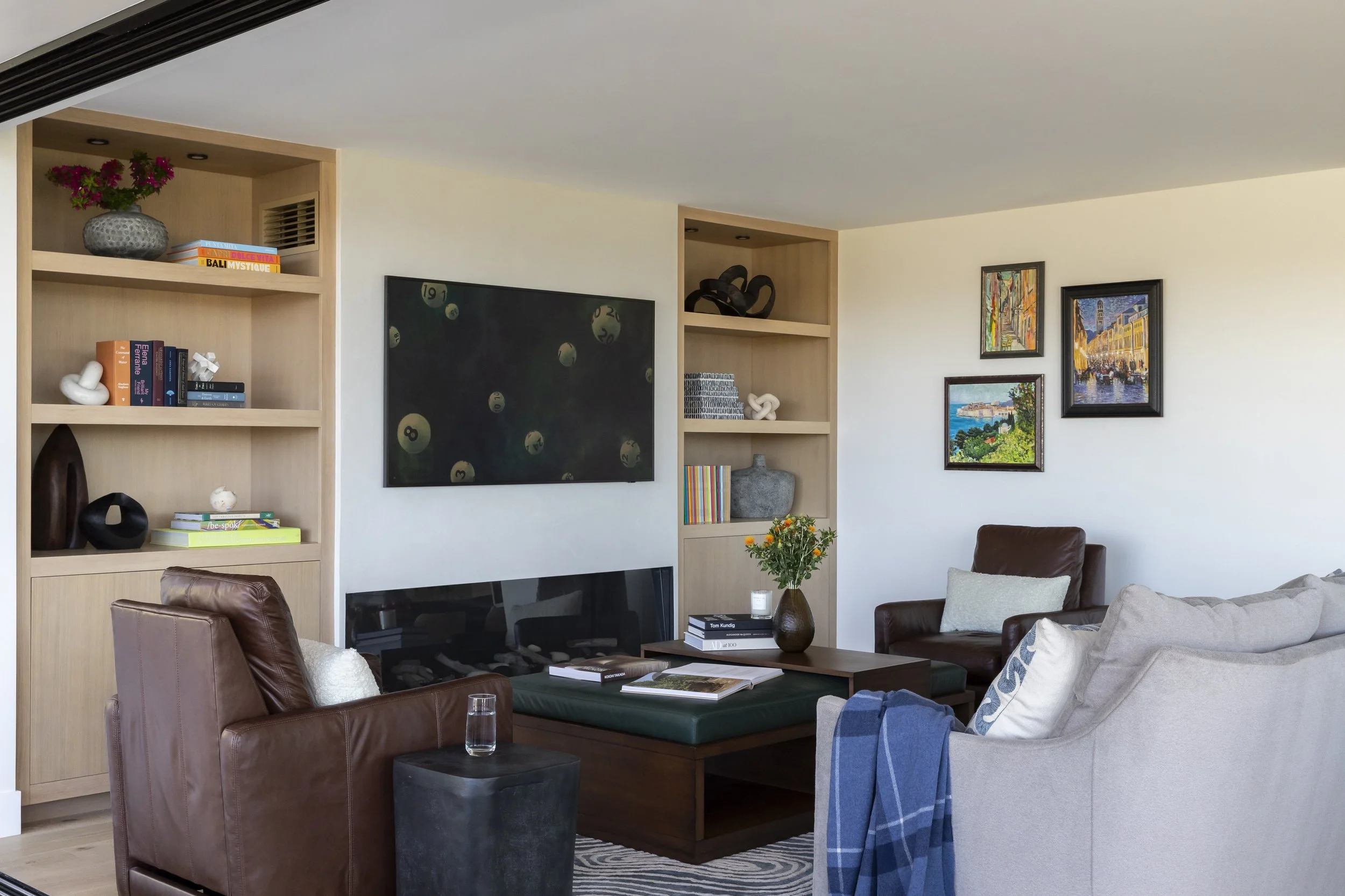 Solana Beach, CA living room design featuring custom built-in shelving, a sleek fireplace, layered seating, and curated artwork for a warm, modern gathering space by Anne Flynn Designs.