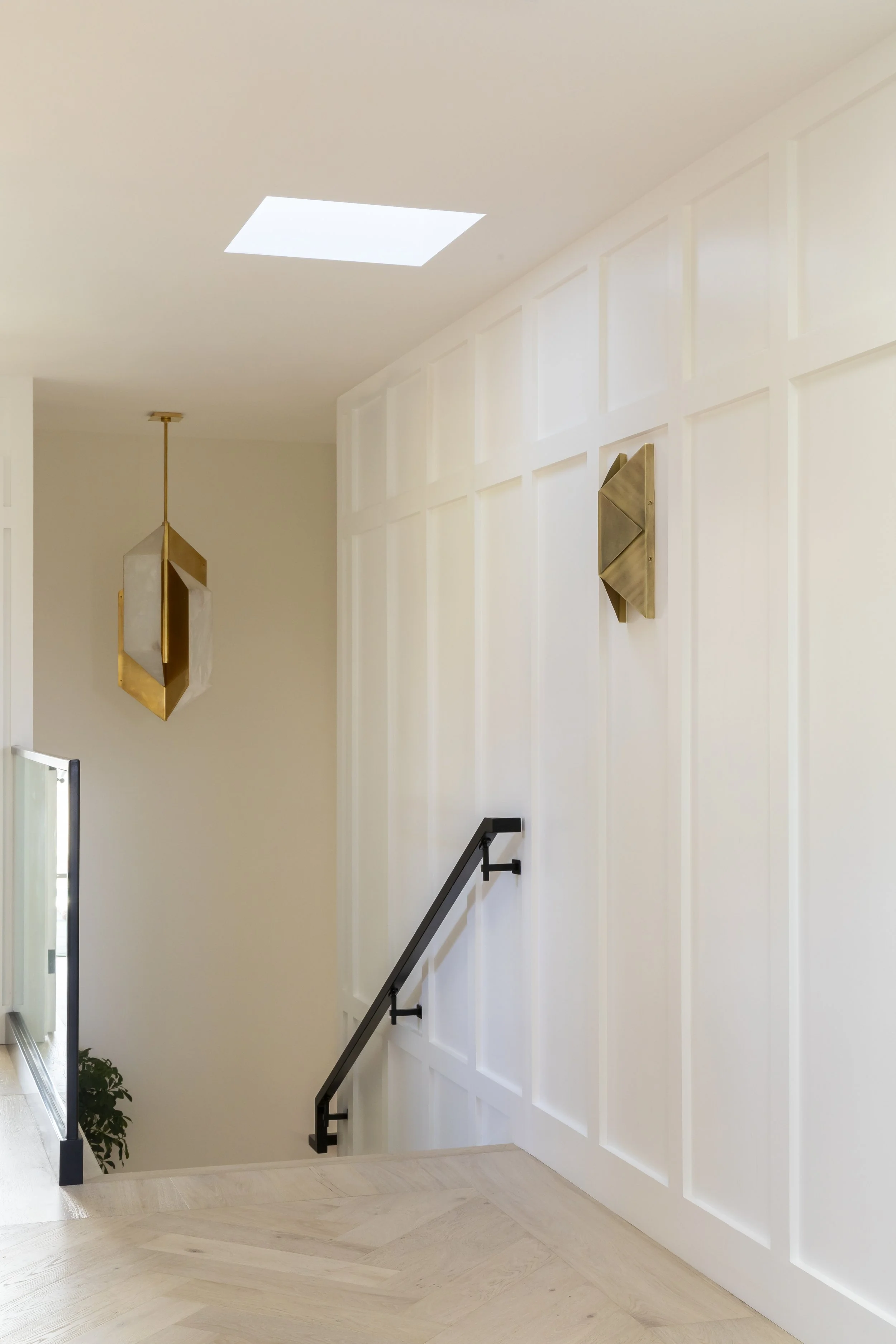 Solana Beach, CA stairwell and hallway design featuring custom paneled walls, sculptural lighting, and clean modern detailing by Anne Flynn Designs.