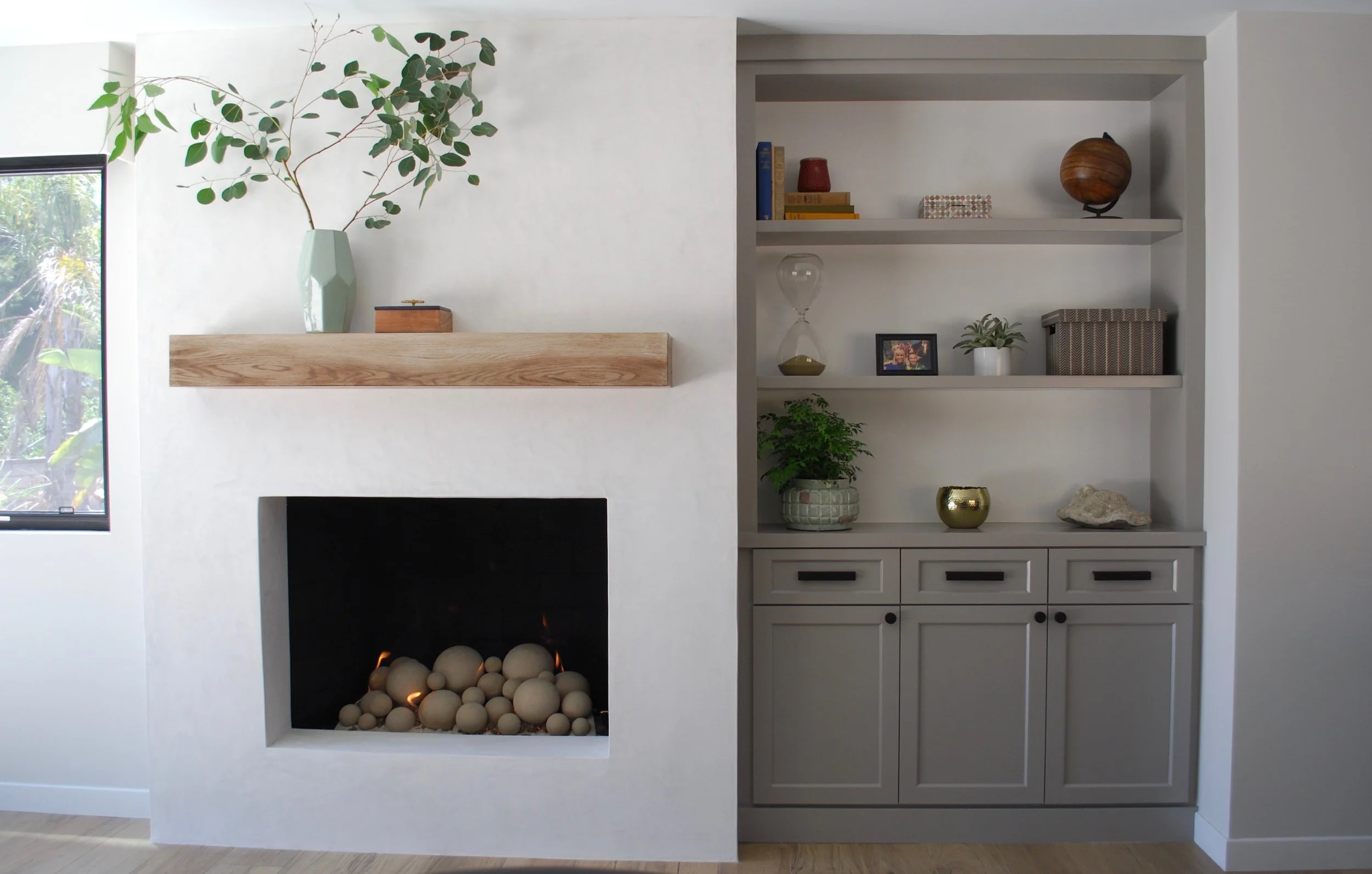 La Costa, CA living room design featuring a custom plaster fireplace, floating wood mantel, and built-in shelving with curated décor for a warm, contemporary aesthetic by Anne Flynn Designs.