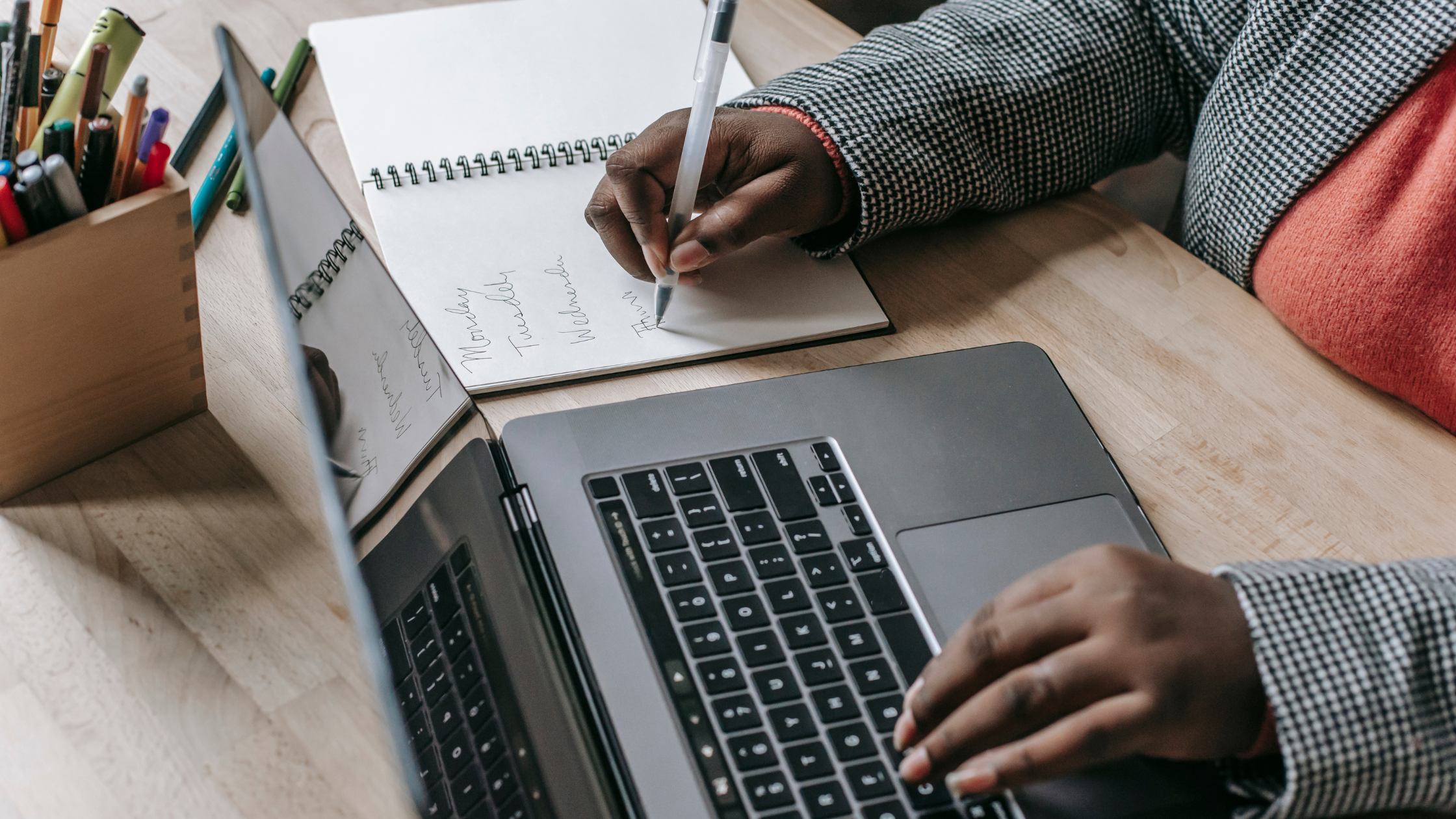 Black person writing notes from a laptop computer