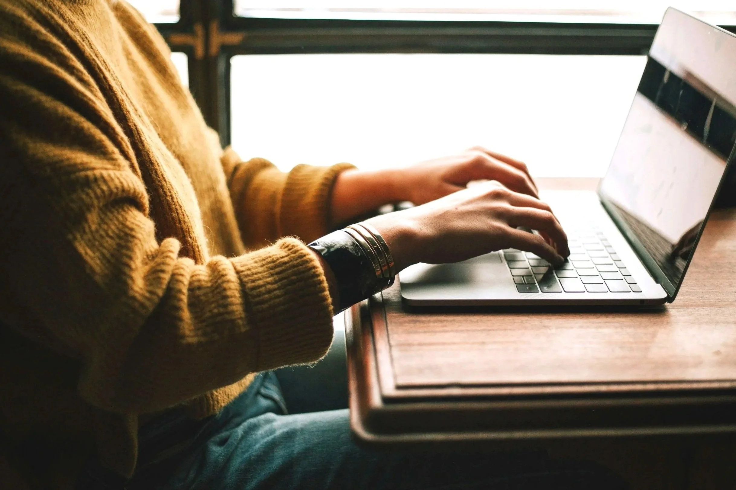 vrouw met gele trui zit aan houten tafel en schrijft een review op haar laptop