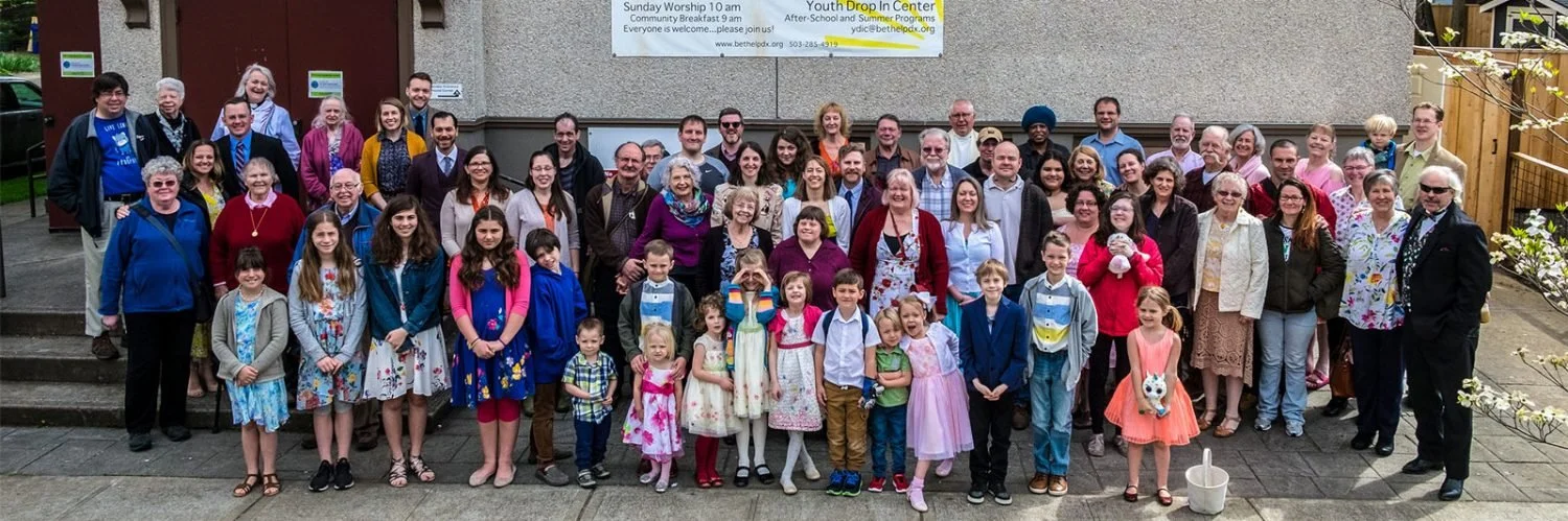 A large group of people gathered outside a building for a photo, including adults and children, with some standing on steps and others on the ground.