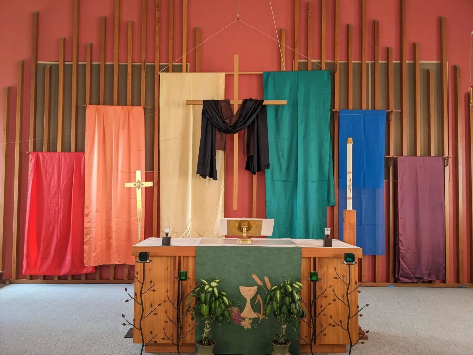 Religious altar with colorful rainbow fabric banners, candle, cross, and plants in a church.