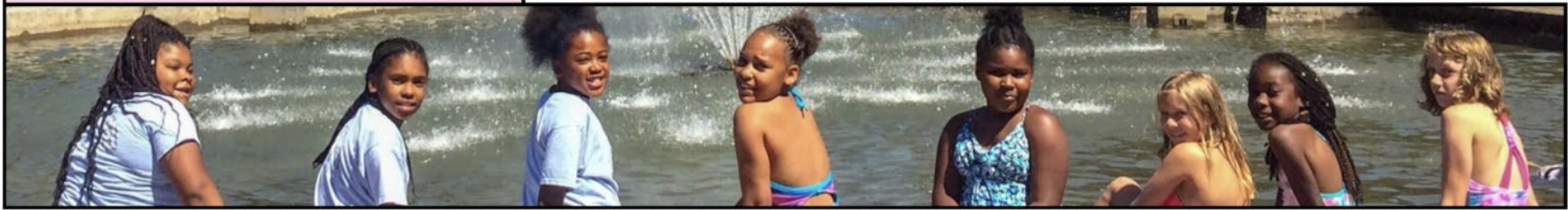 Children playing in a water fountain or pond, dressed in summer clothing, with a water feature in the background.