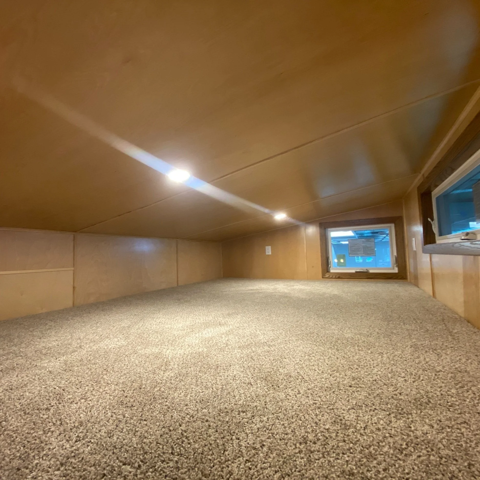 Interior of a small, carpeted loft with low ceiling, recessed lighting, and windows.