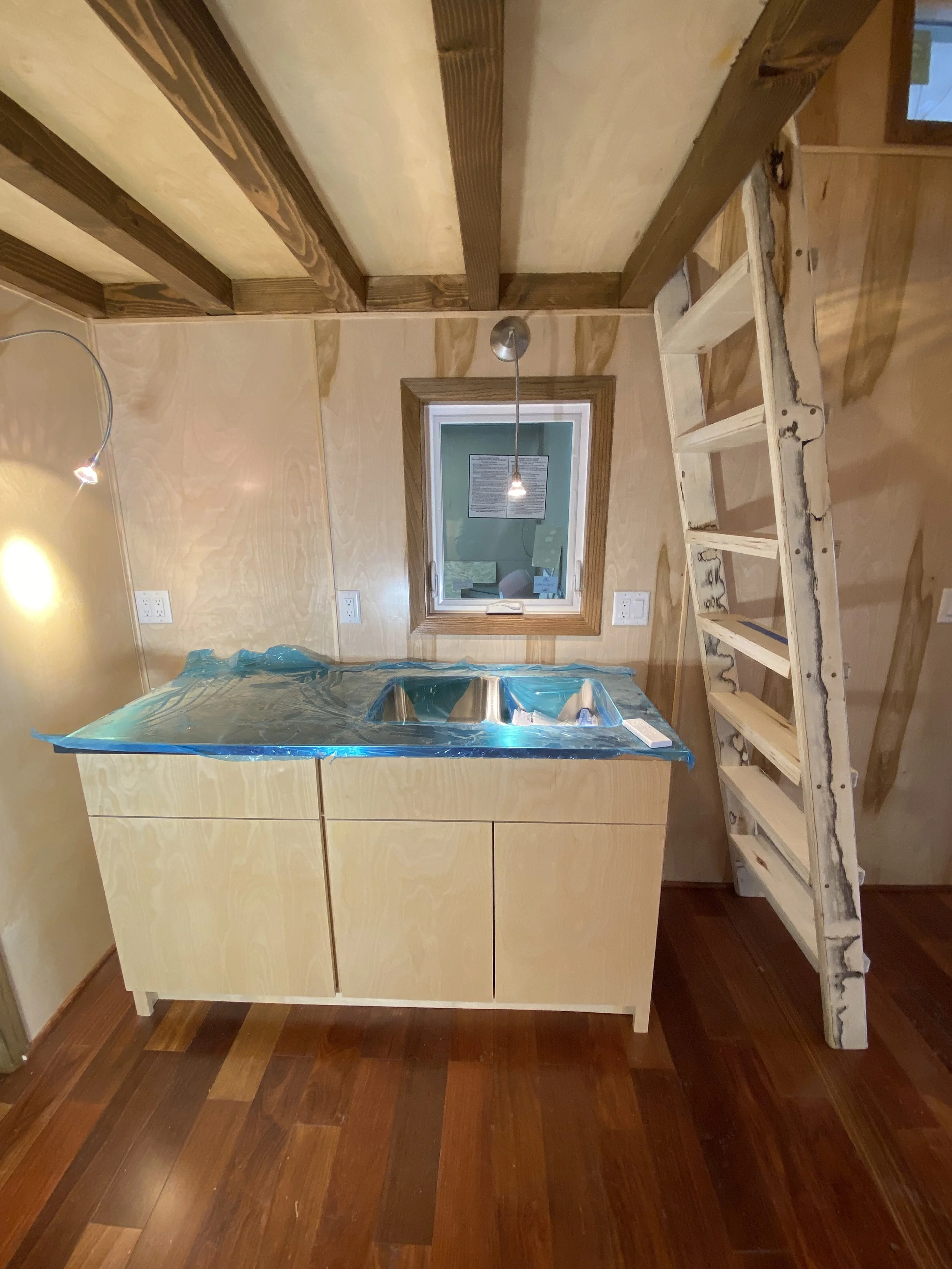 Small wooden kitchen with a loft-style ladder, exposed ceiling beams, sink, and pendant light.