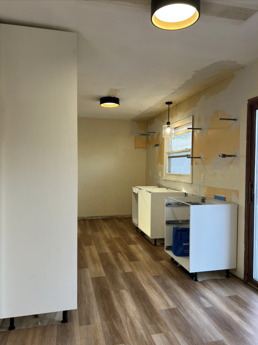 Kitchen under renovation with unfinished cabinets, bare walls, and exposed lights.