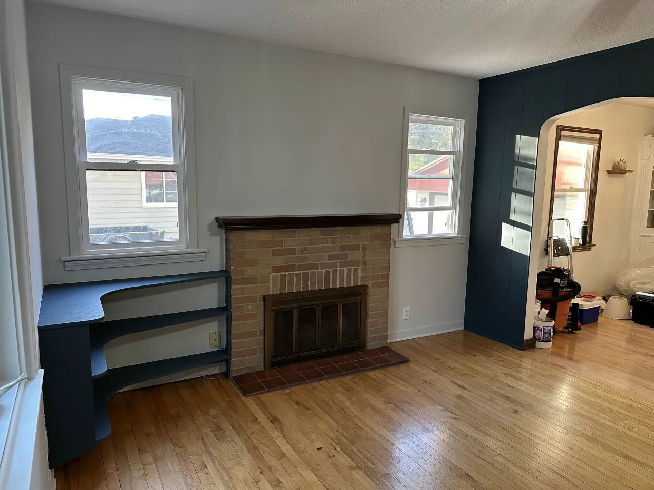 Living room with a brick fireplace, hardwood floor, arched doorway, built-in shelving, and windows providing natural light.