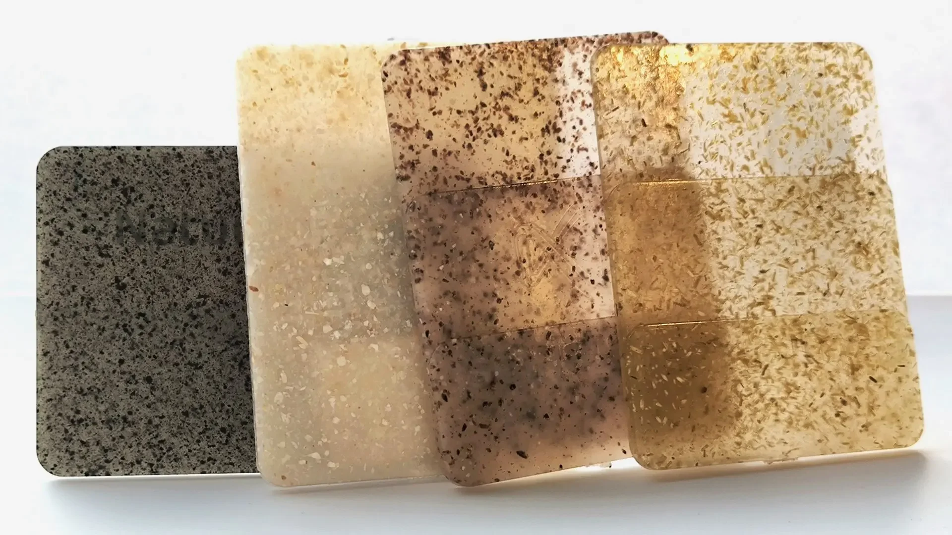 Four types of soap stacked in a staggered arrangement: black with speckles, beige with speckles, brown with darker speckles, and golden with flecks.