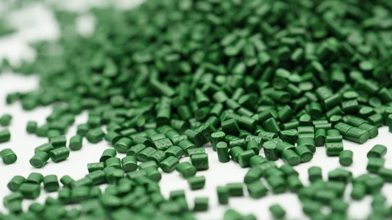 Close-up of scattered green plastic pellets or granules on a white surface.