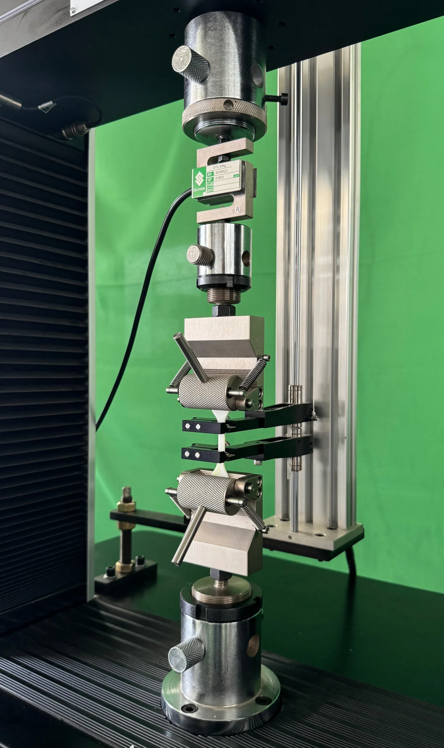 Close-up view of a mechanical laboratory instrument with metallic components, mounted on a base, against a green background.