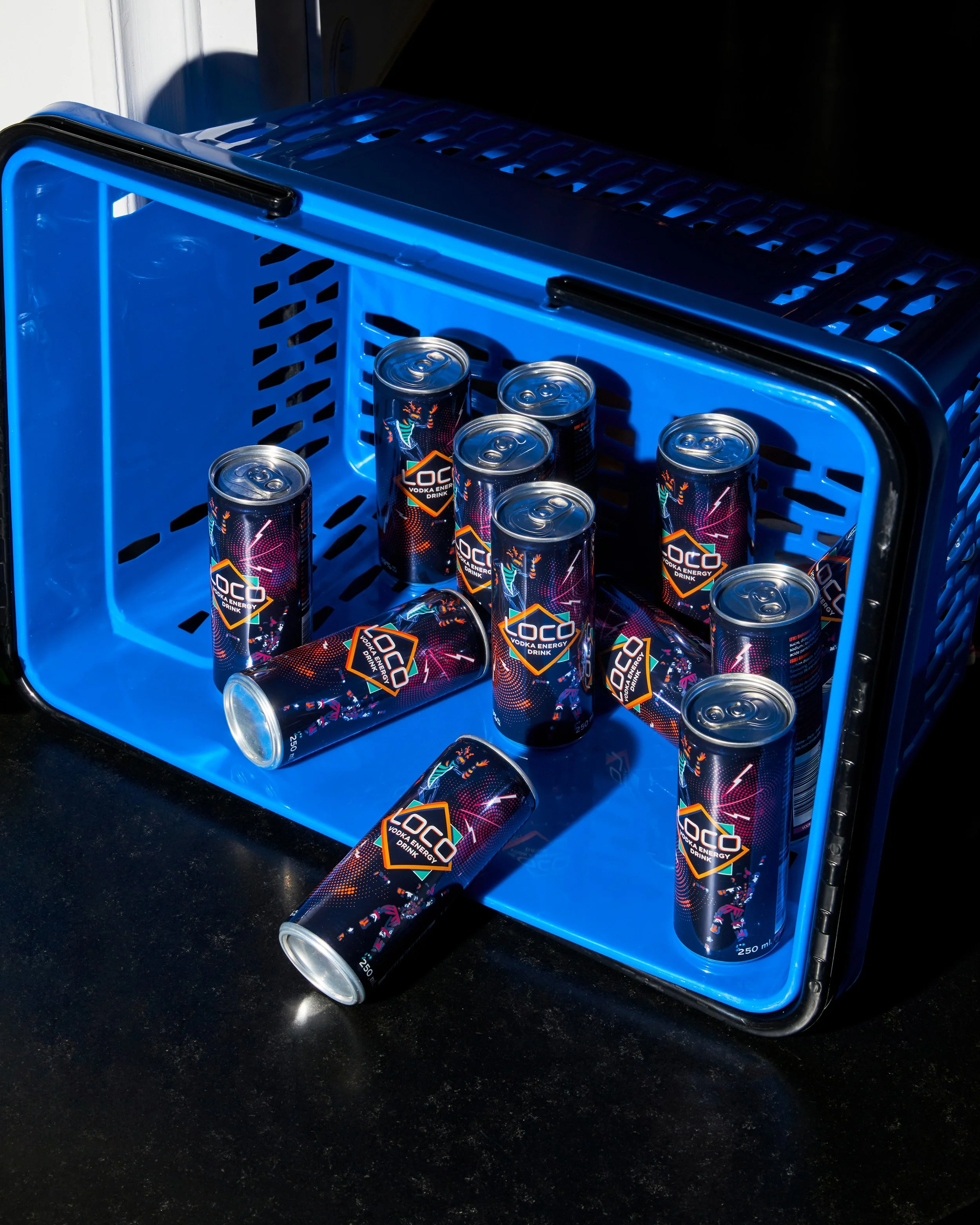 Canettes de boisson énergisante 'LOCO' dans une boîte bleue, certaines tombant par terre.