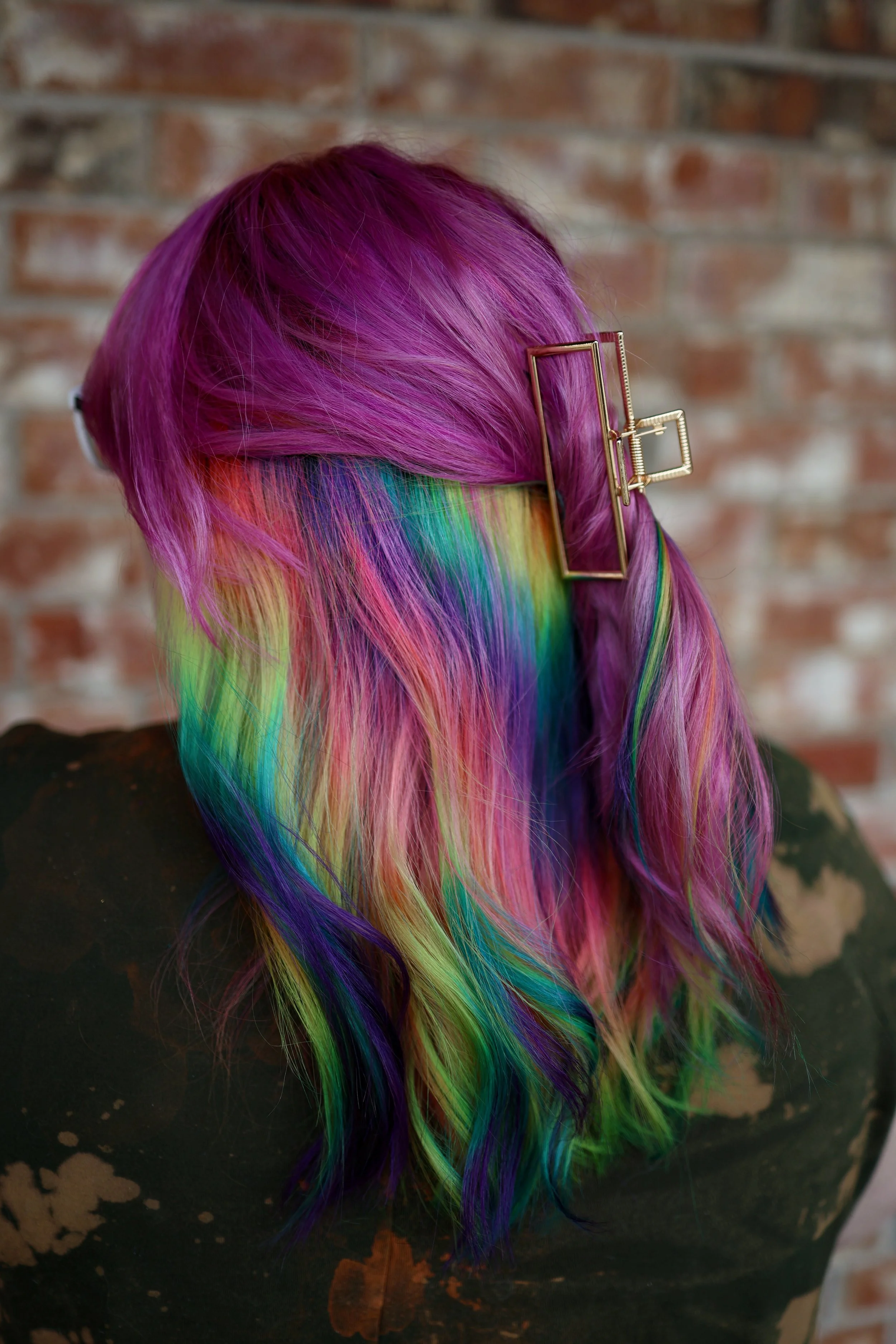 person with medium length pink fuschie hair with a peekaboo halo of rainbow prism in bright purples, pinks, blues, and yellows underneath