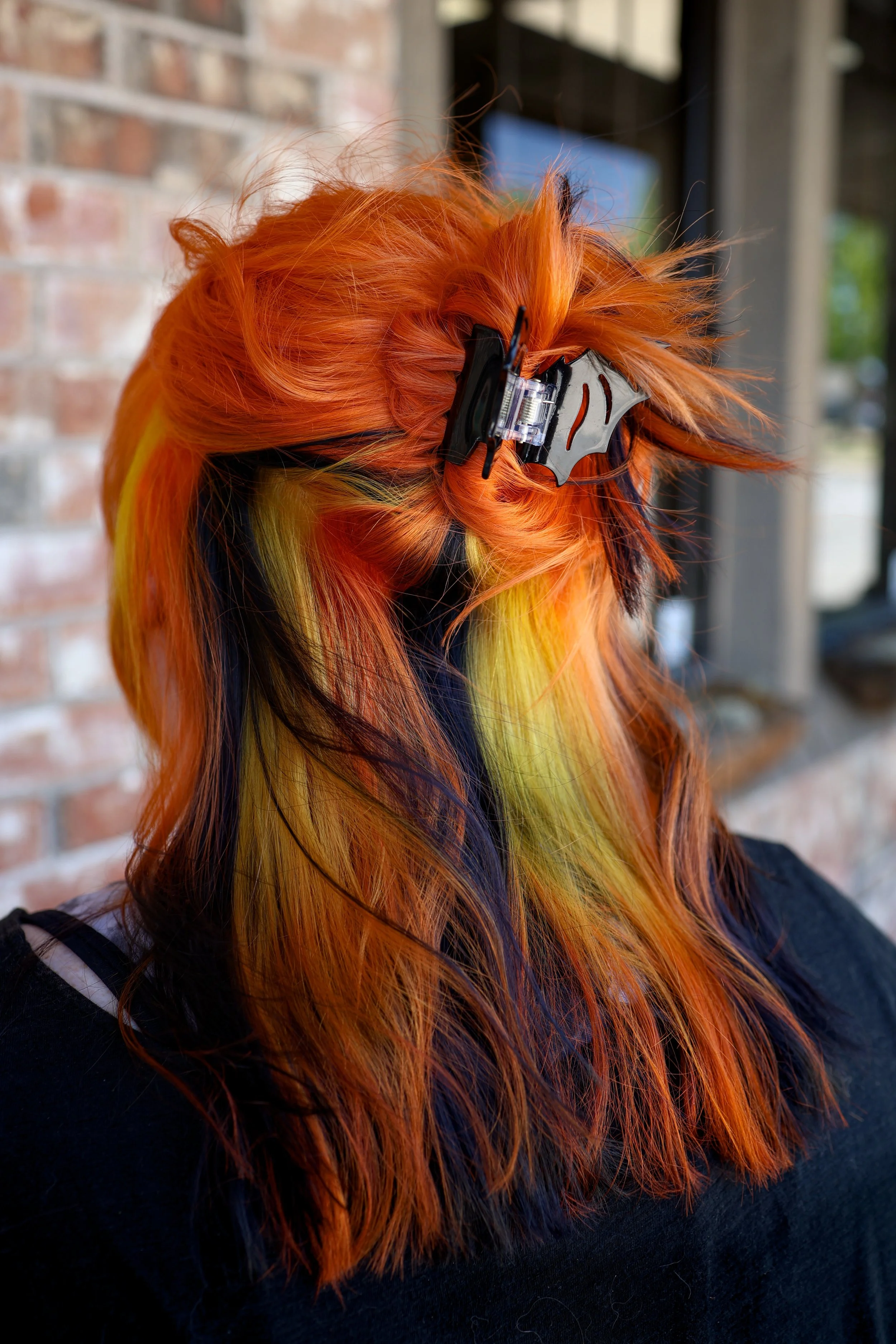 person with medium length bright orange hair with a peekaboo of orange, black and yellow stripes underneath