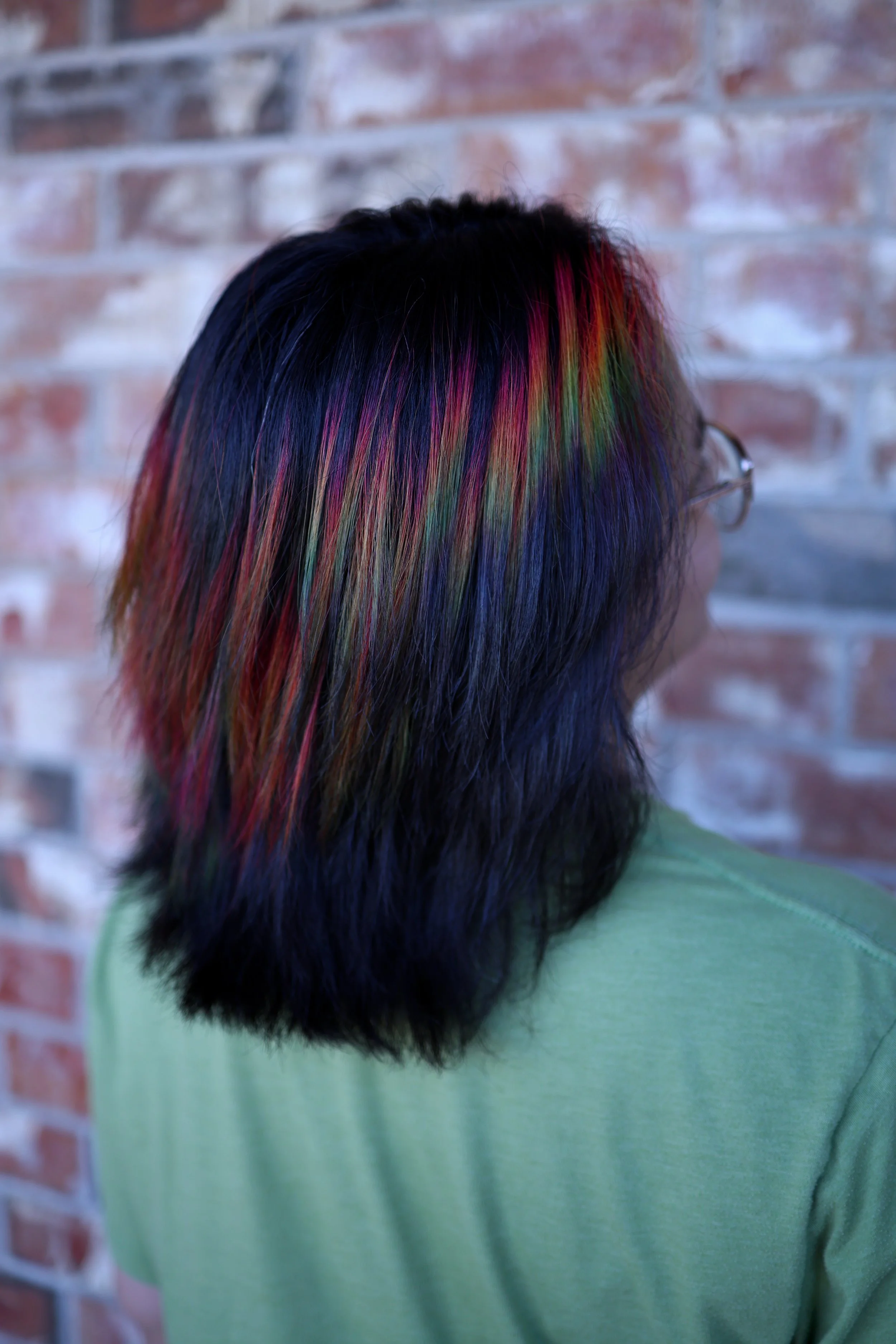 person with shoulder length natural brown hair with a rainbow prism shine line