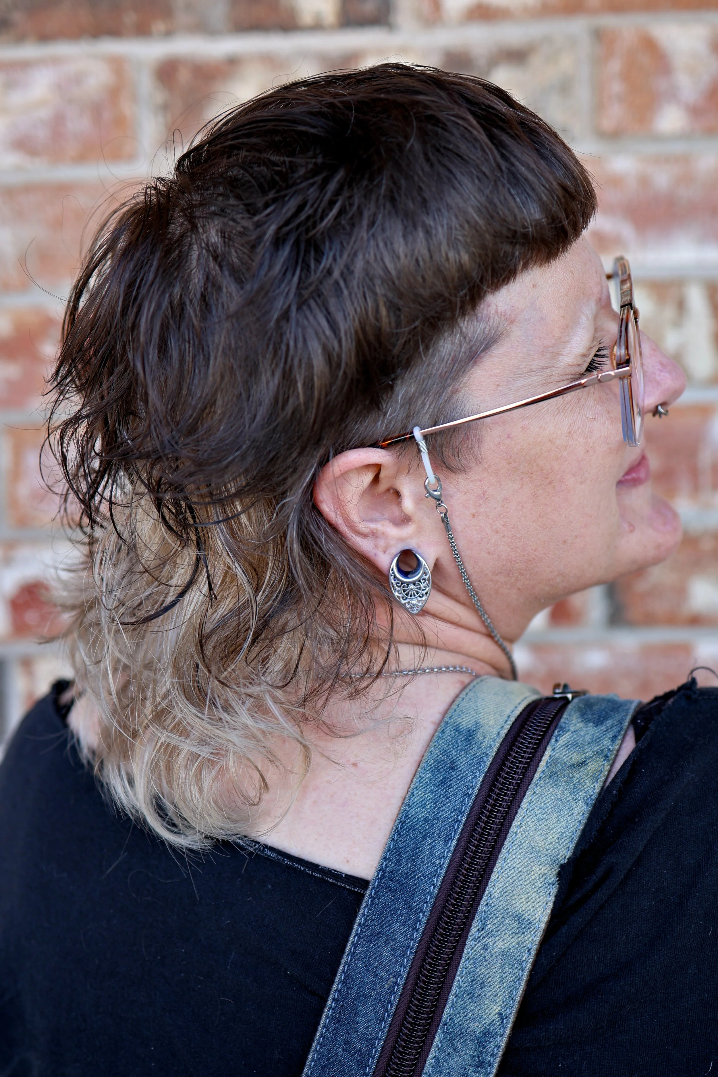 person with a textured wavy mullet with natural brown color on top and color block chunks of blonde throughout and baby bangs