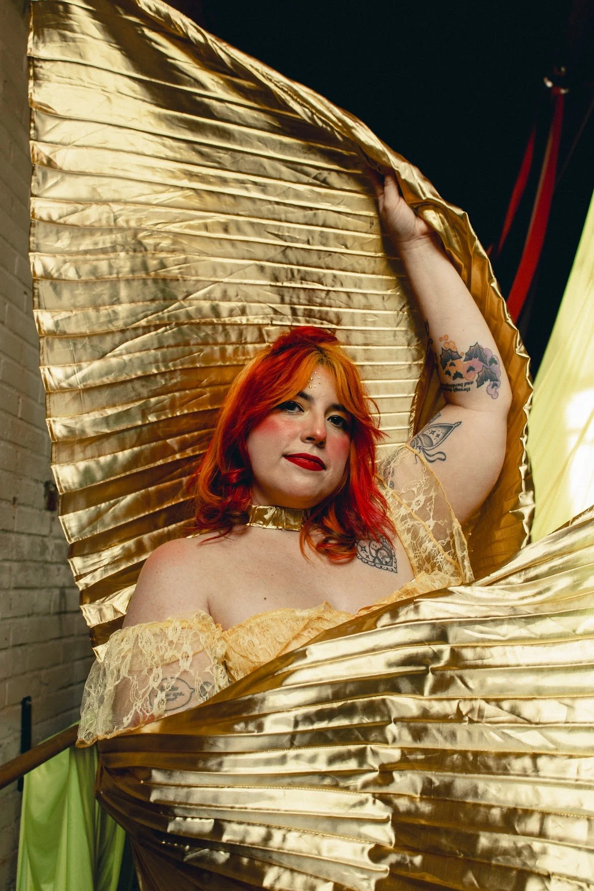 Woman with red yellow and brown hair pulled up into a half up hairstyle inspired by Gene Simmons from KISS and a gold corset and gold wings inspired by Belle from Beauty and the Beast