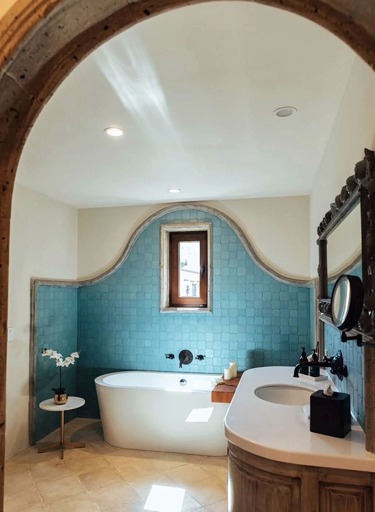 Bathroom with blue tiles, bathtub under a window and the bathroom sink with mirror in Hotel El Golpe de Vista in San Miguel de Allende.