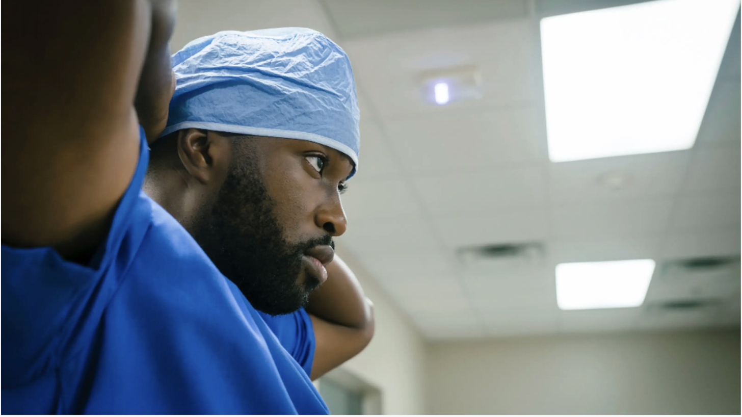 A male healthcare worker in surgical scrubs and a cap, preparing for surgery in a hospital operating room.