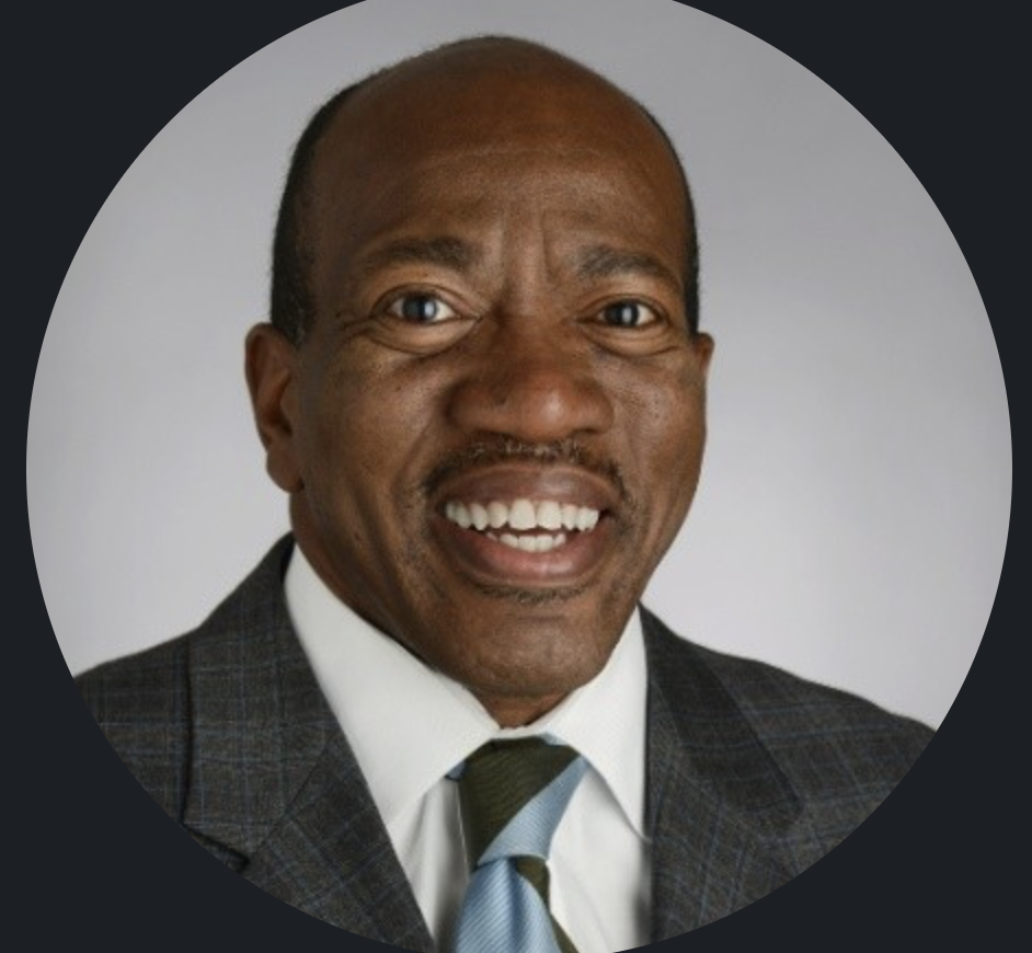 Portrait of a smiling middle-aged African American man in a suit and tie against a plain background.